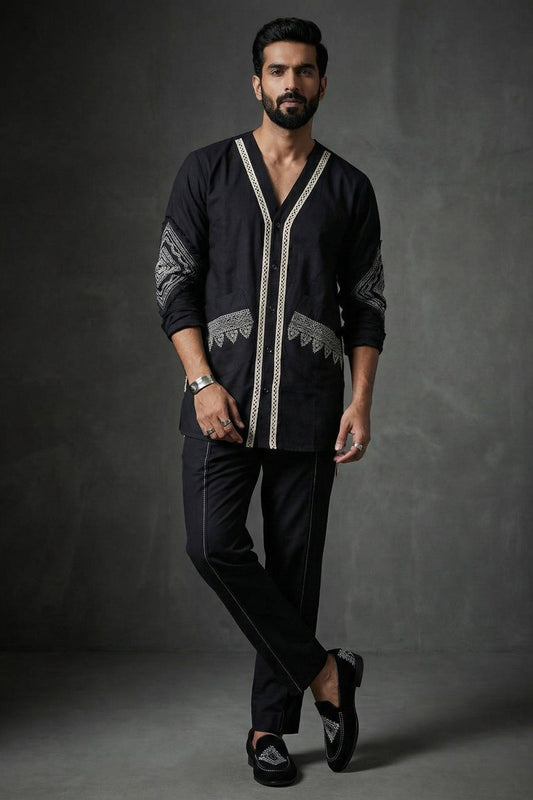 Man wearing a black embroidered shirt and pants against a dark background