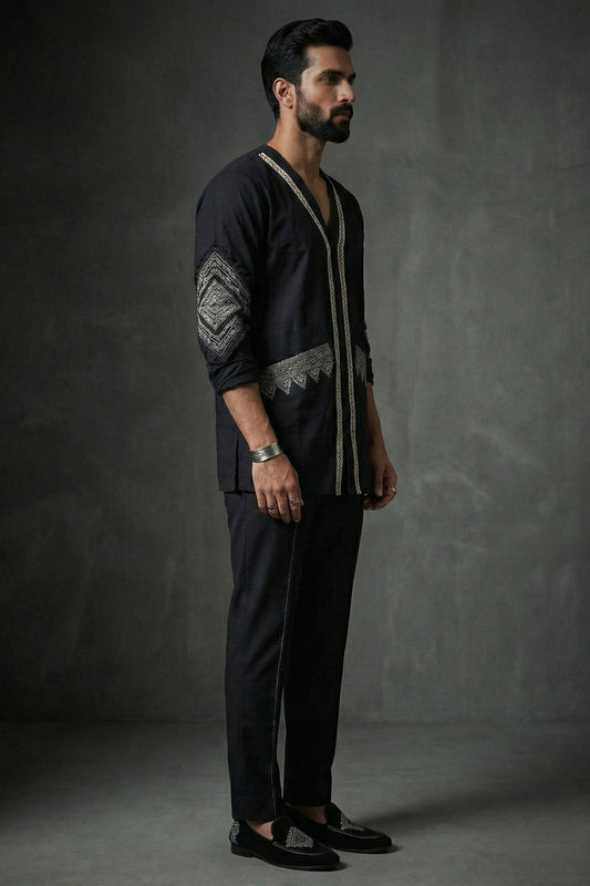 Man wearing a dark outfit with intricate patterns against a gray background