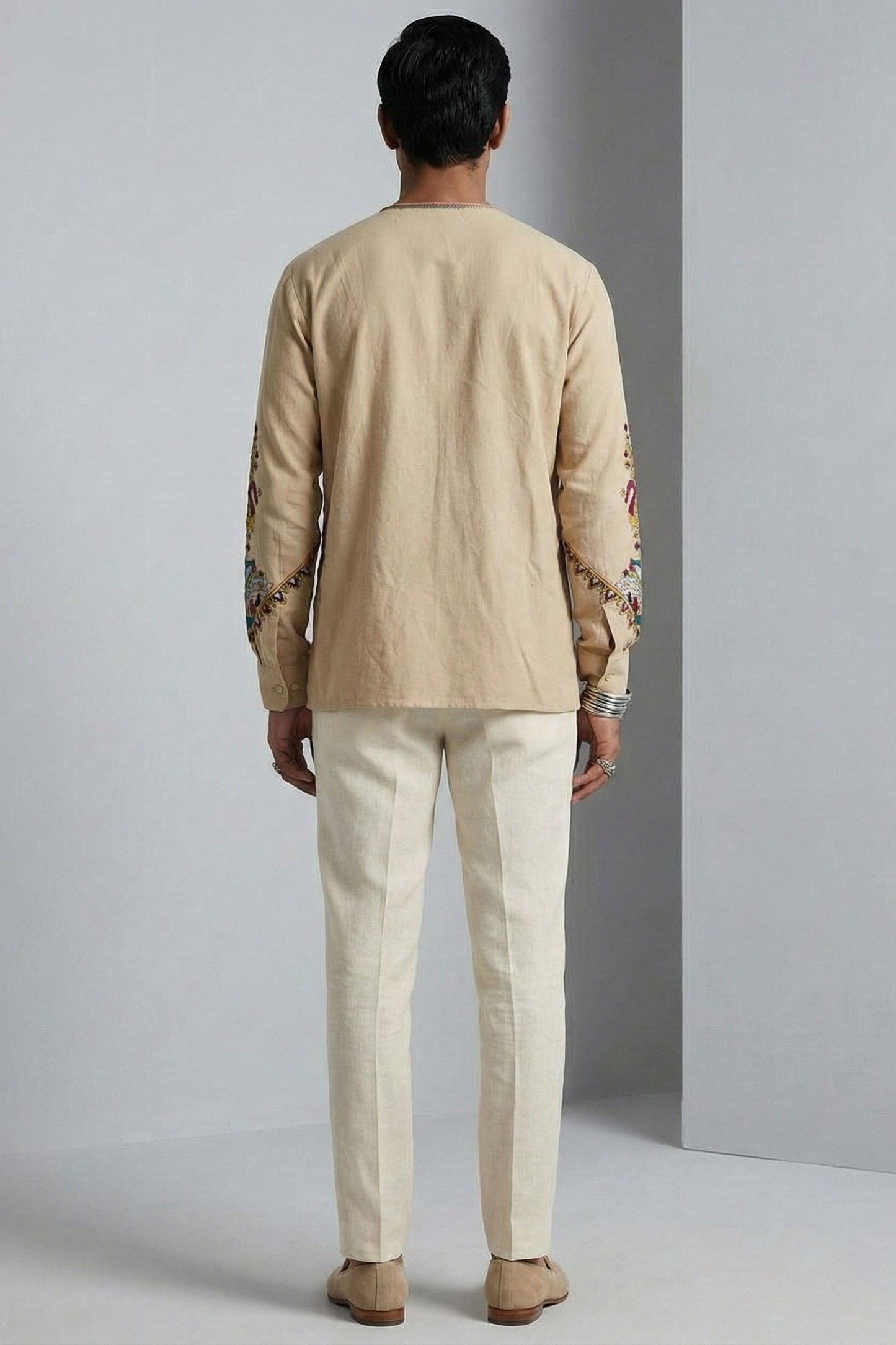 Man wearing a beige embroidered shirt and pants against a gray background