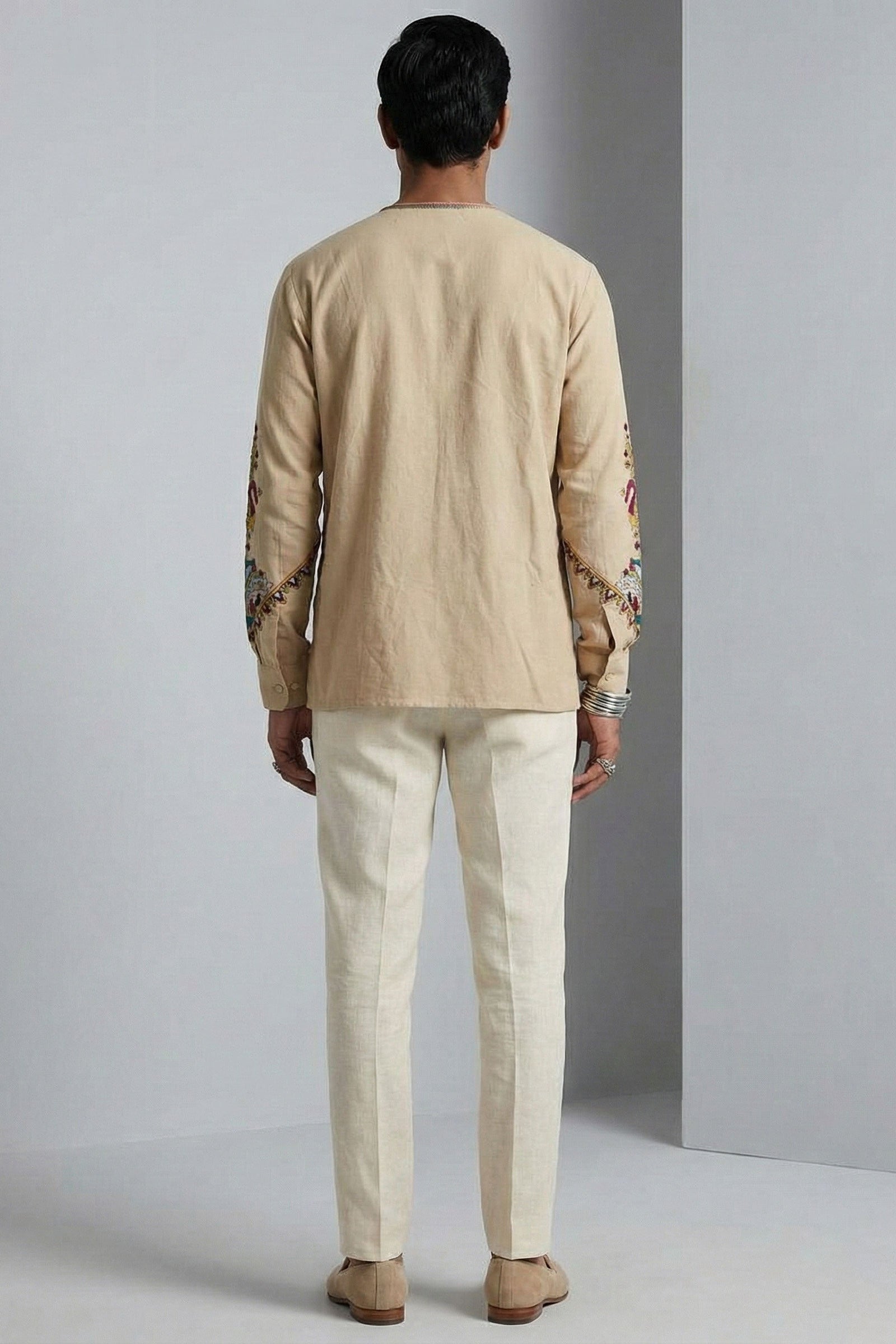 Man wearing a beige embroidered shirt and pants against a gray background