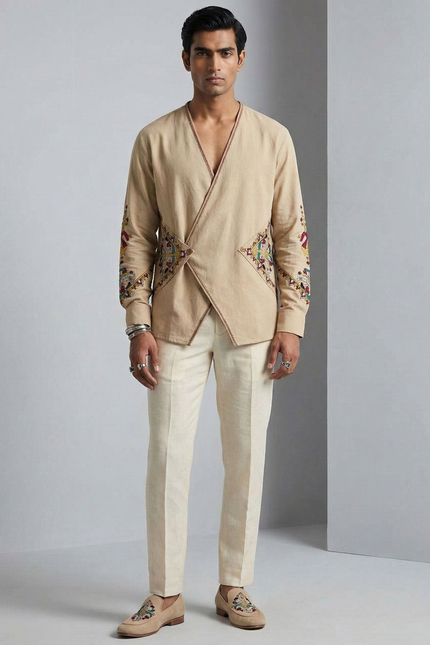 Man wearing a beige embroidered jacket and pants against a gray background