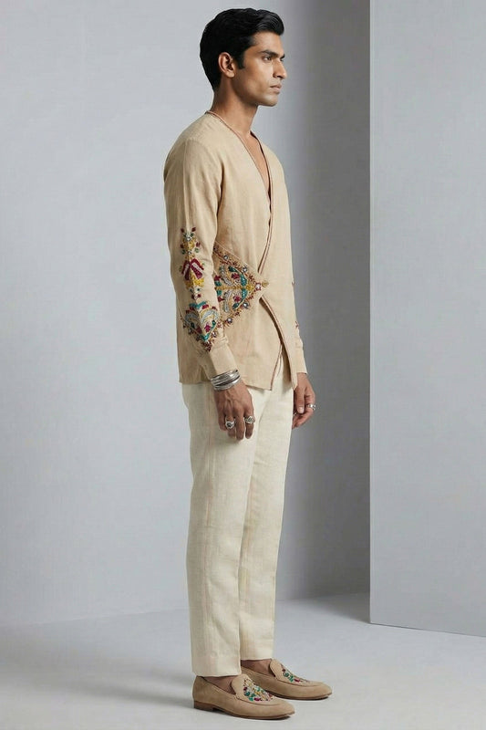 Man wearing a beige embroidered jacket and pants against a gray background