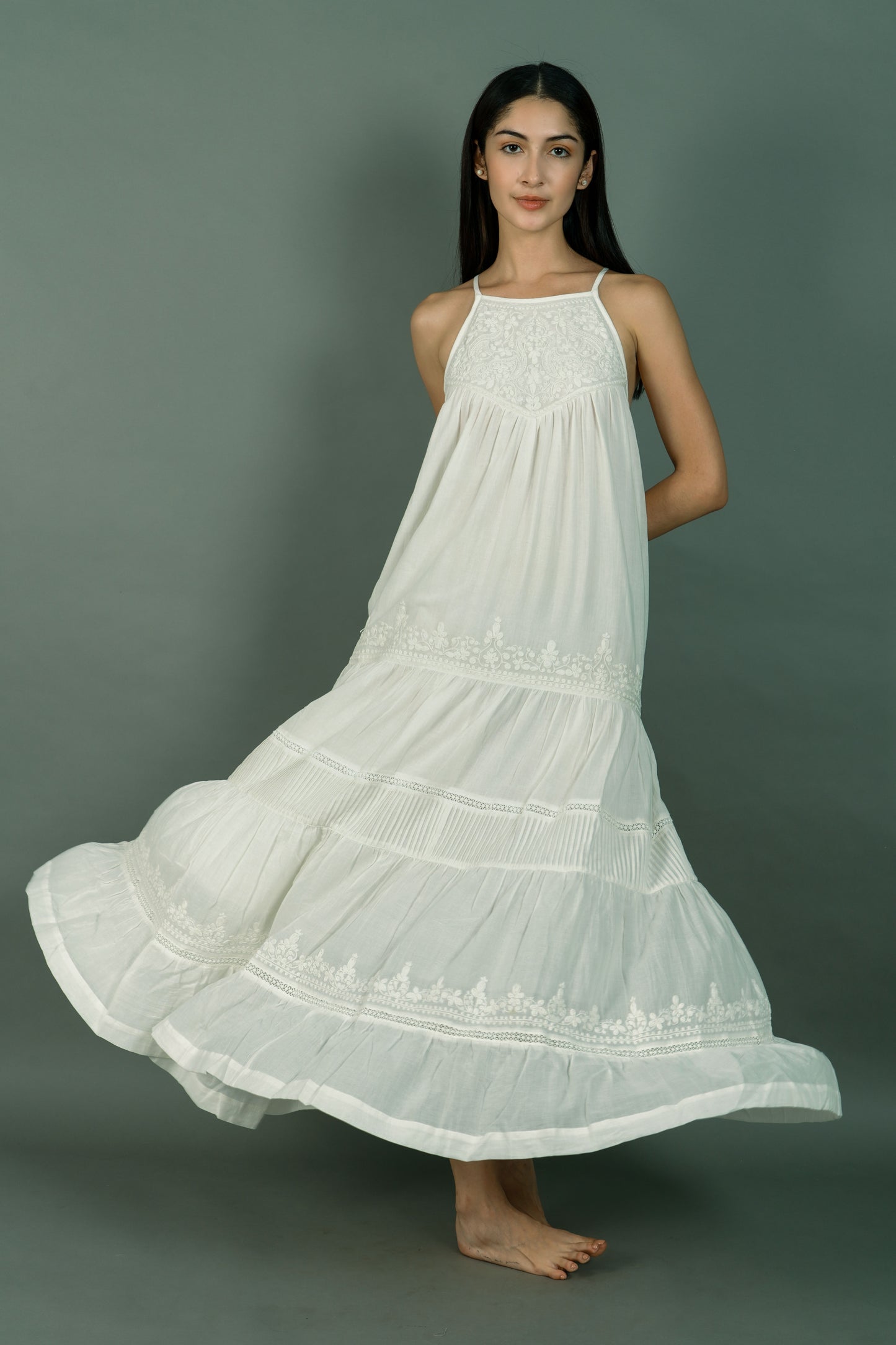 Woman wearing a long white dress with intricate patterns on a gray background