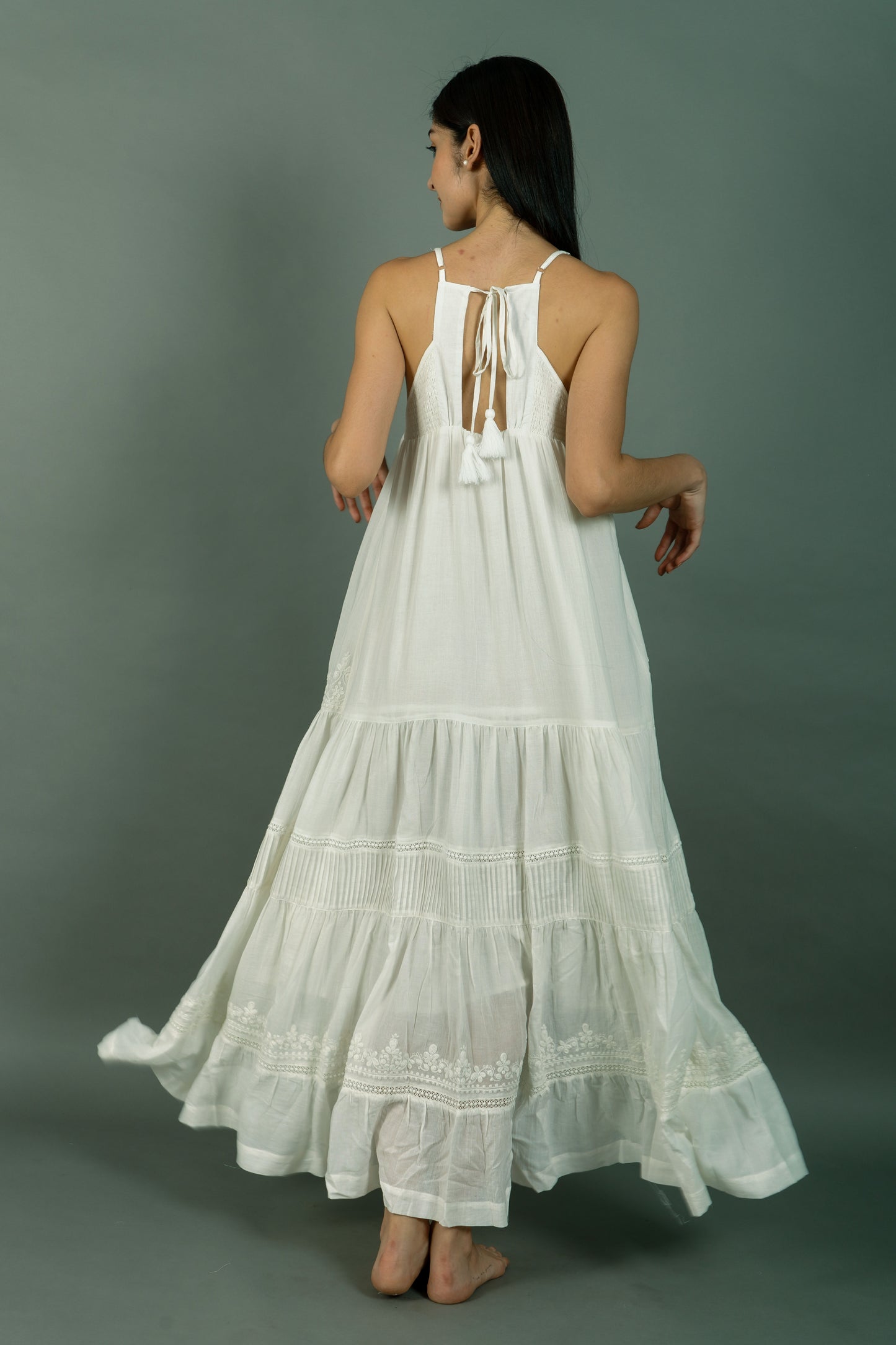 Woman wearing a white dress with tiered skirt and lace details on a gray background