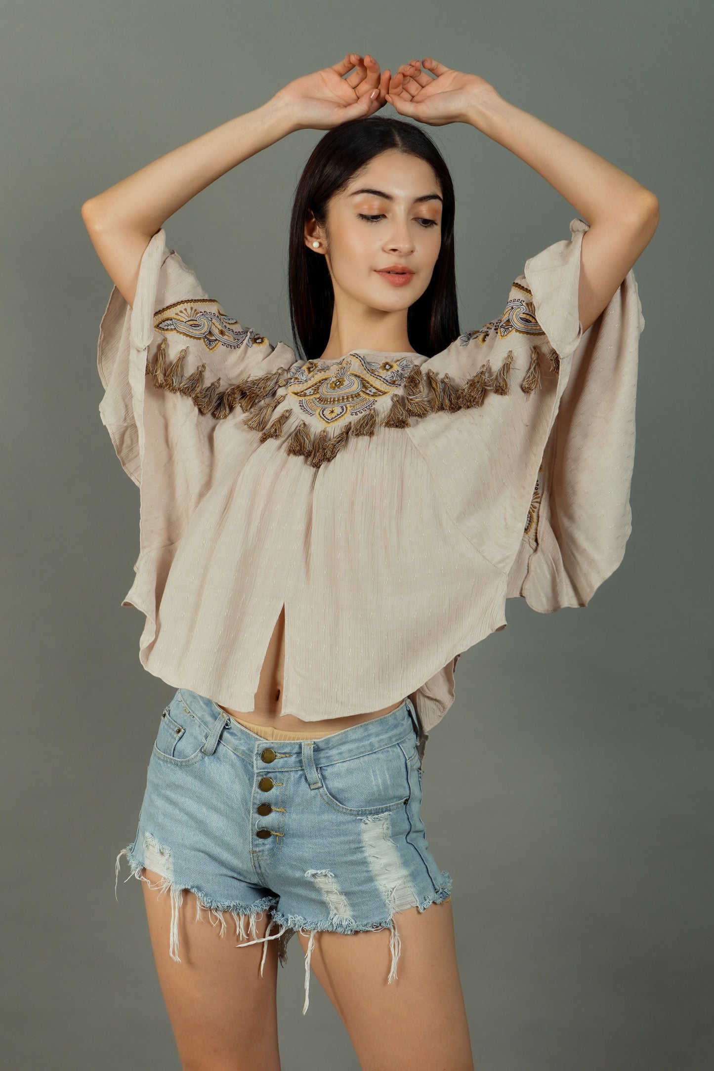 Woman wearing a beige blouse with lace details and denim shorts against a gray background