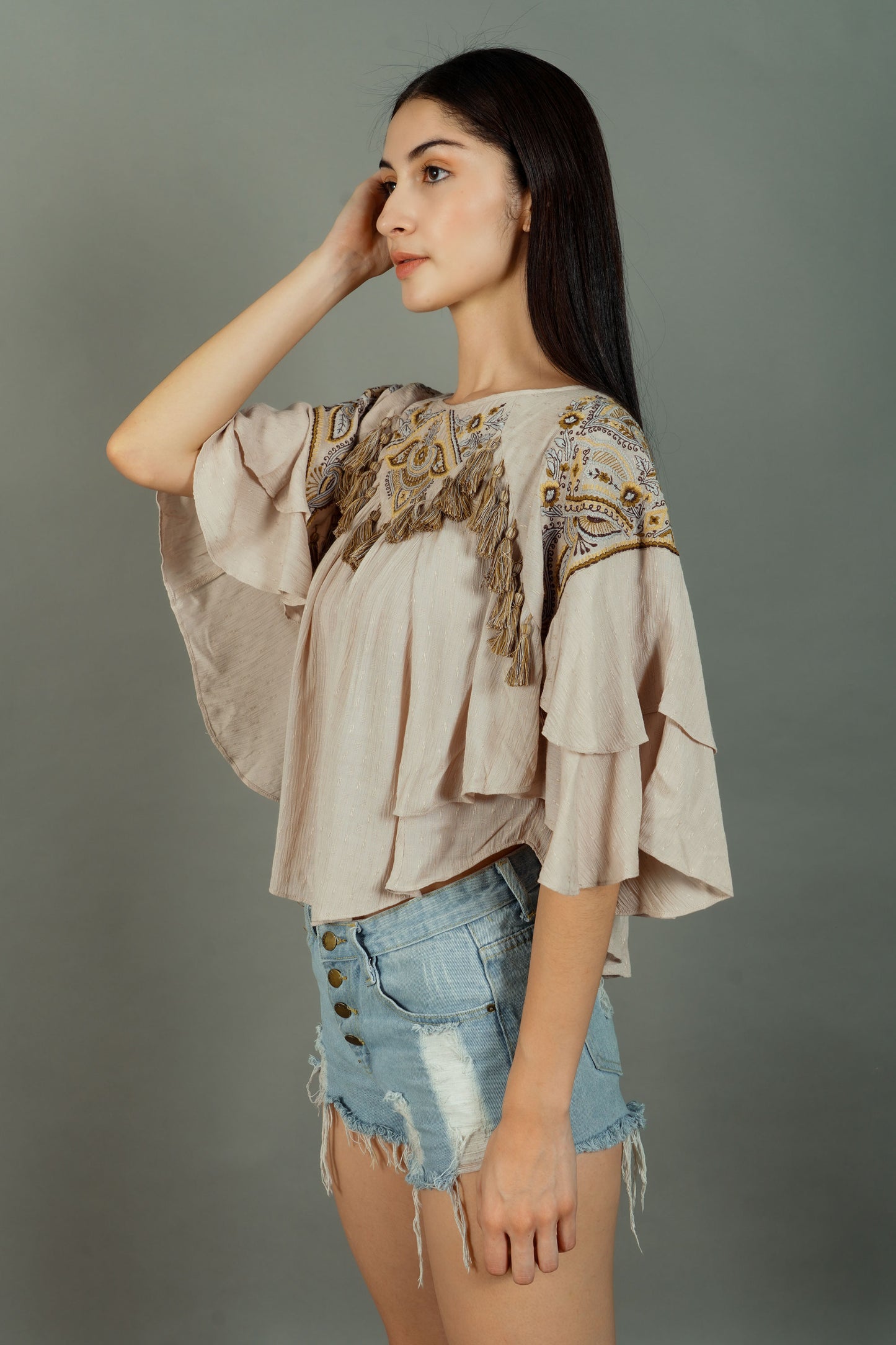 Woman wearing an embroidered top and denim shorts against a gray background