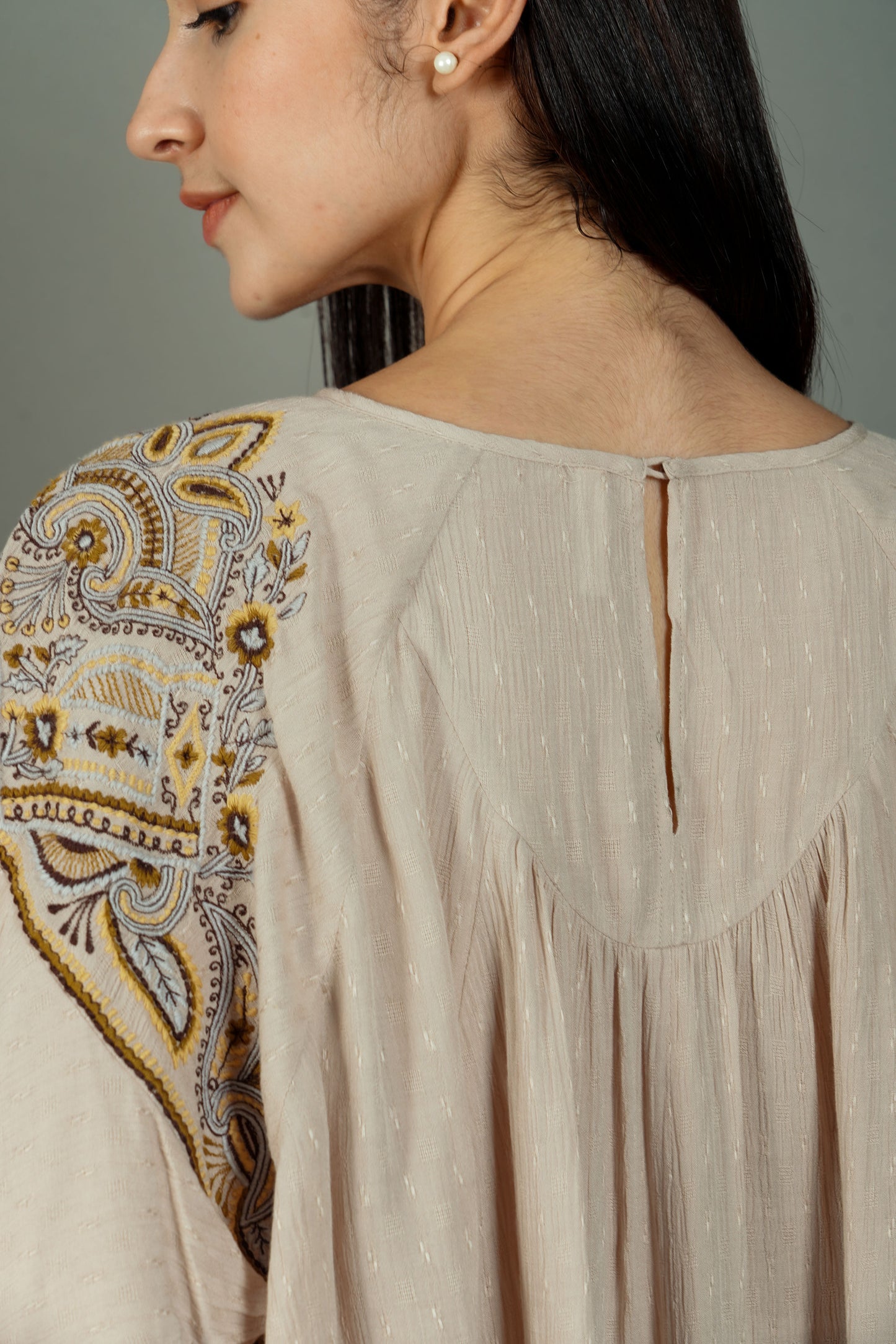 Close-up of a beige blouse with intricate embroidery on the shoulder, worn by a person.