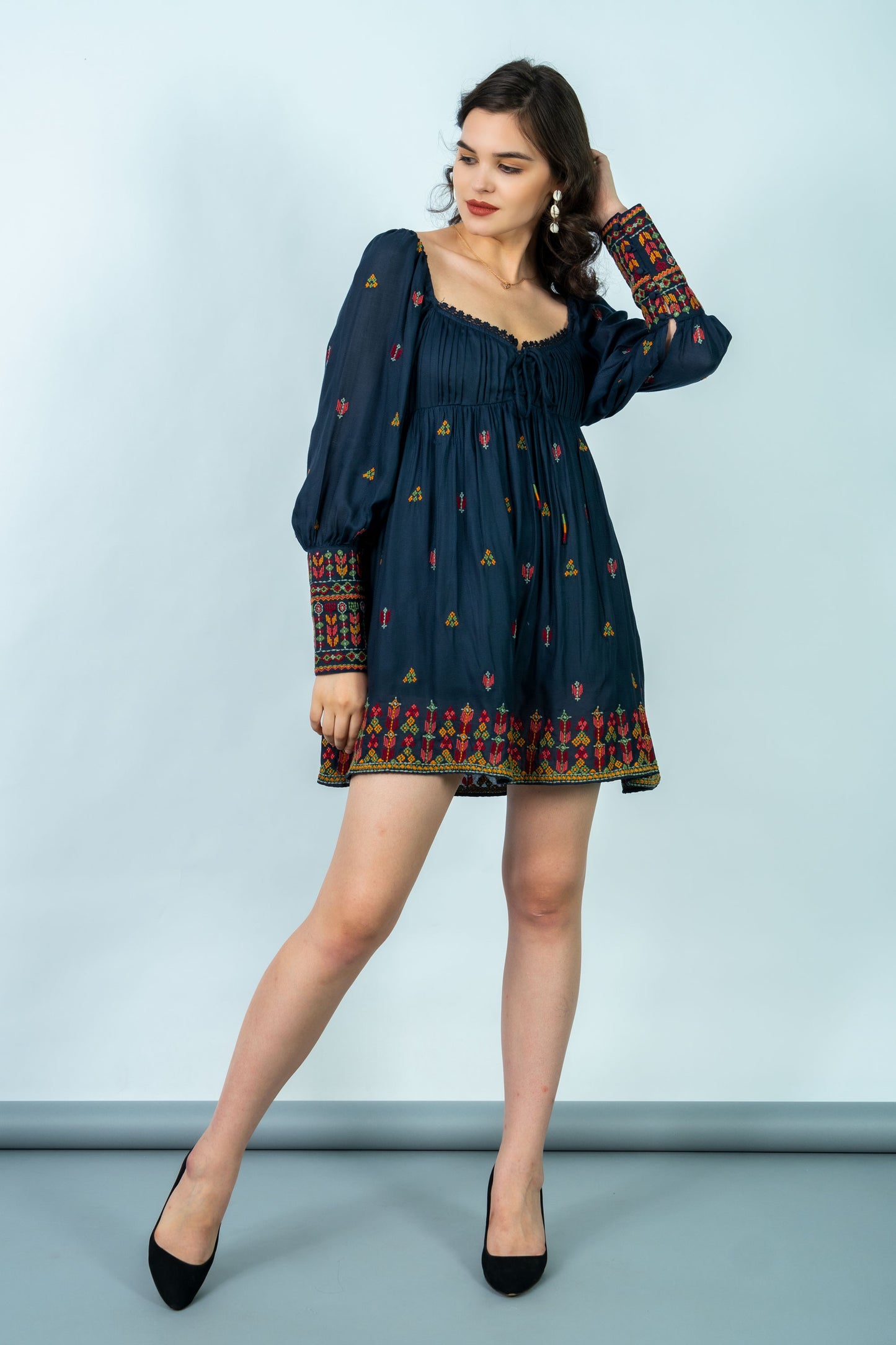 Woman wearing a dark blue dress with patterned long sleeves against a light gray background