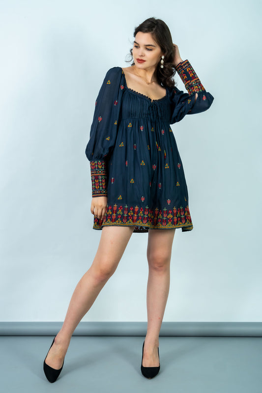 Woman wearing a dark blue dress with patterned long sleeves against a light gray background