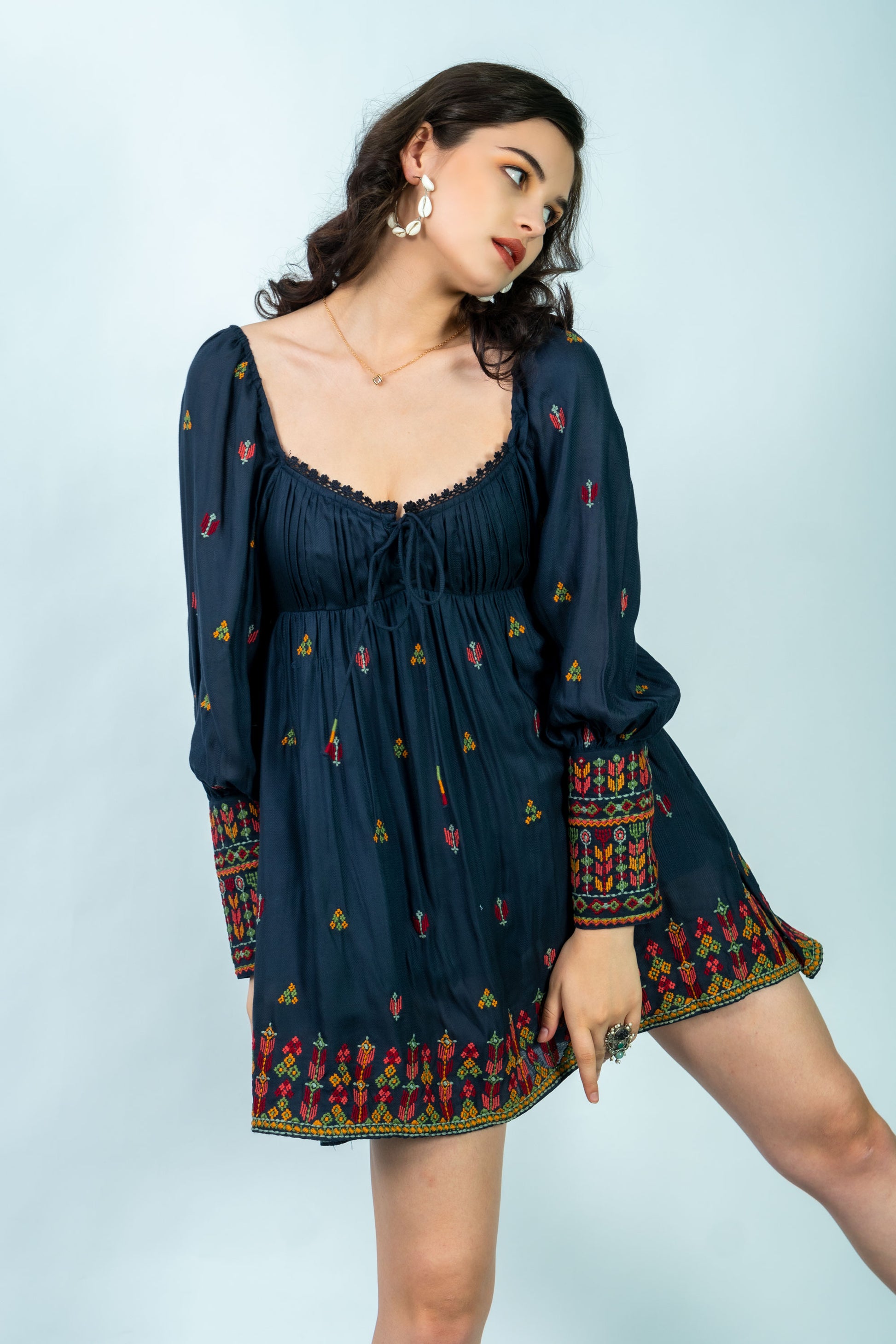 Woman wearing a dark blue dress with colorful patterns on a light gray background