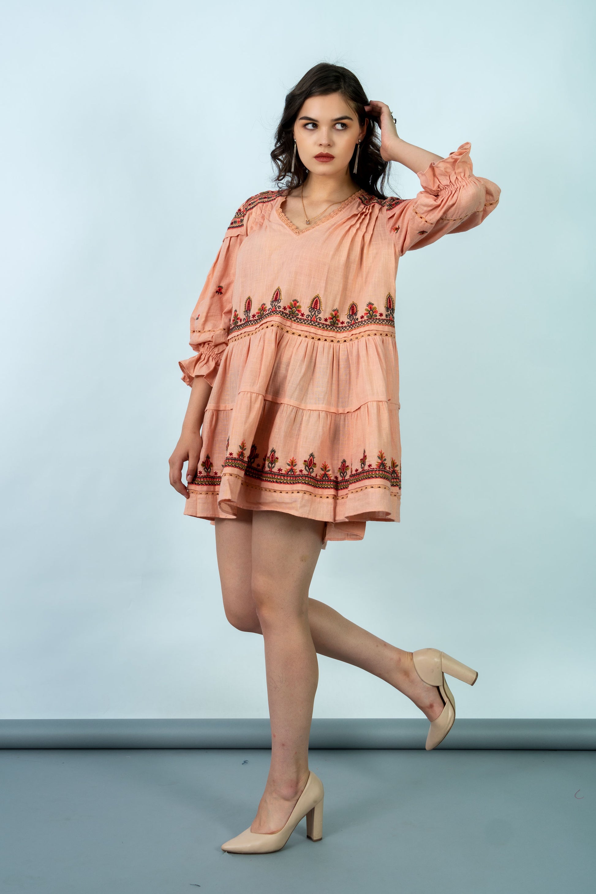 Woman wearing a peach dress with a patterned hem against a light blue background