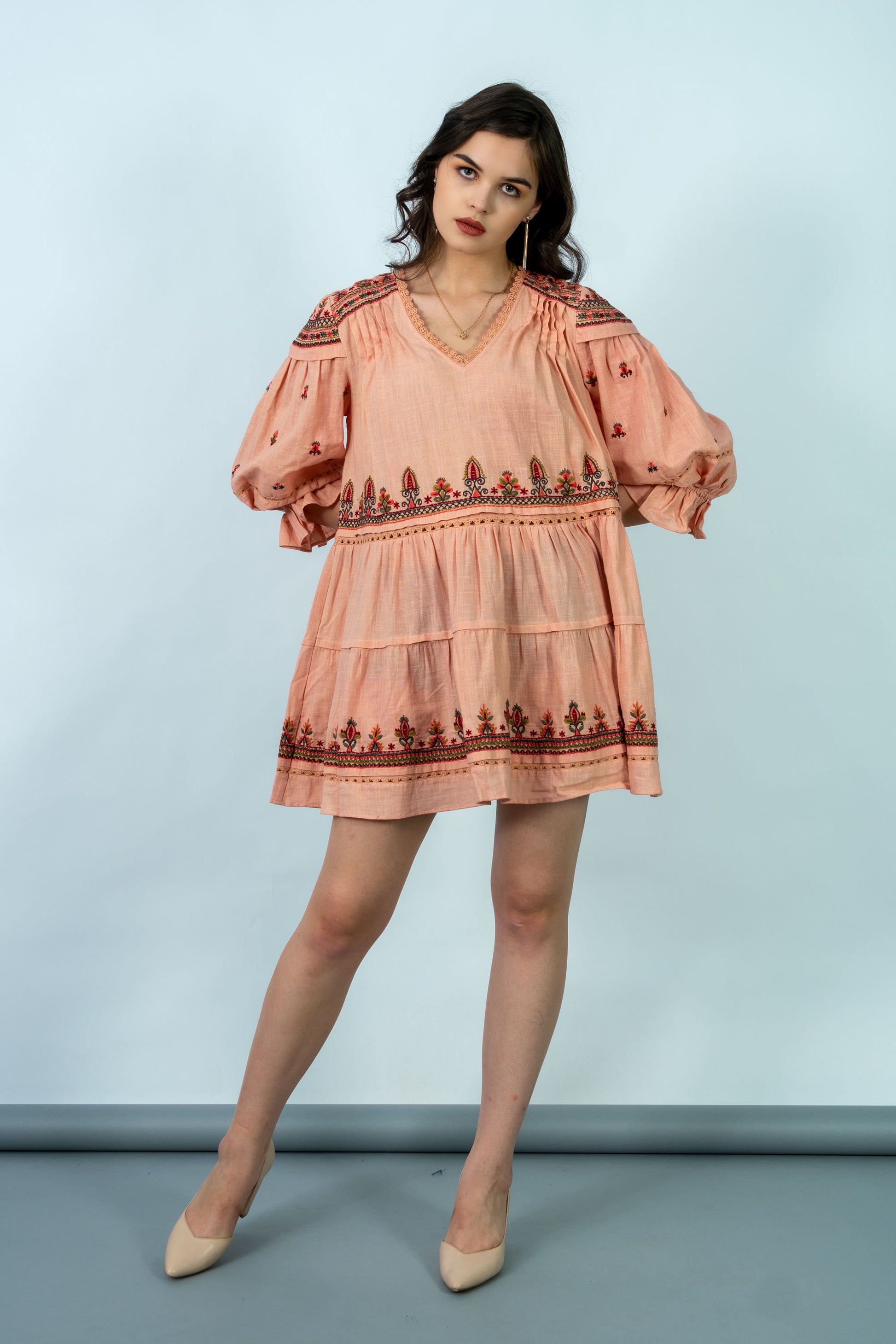 Woman wearing a peach-colored dress with intricate patterns against a light blue background