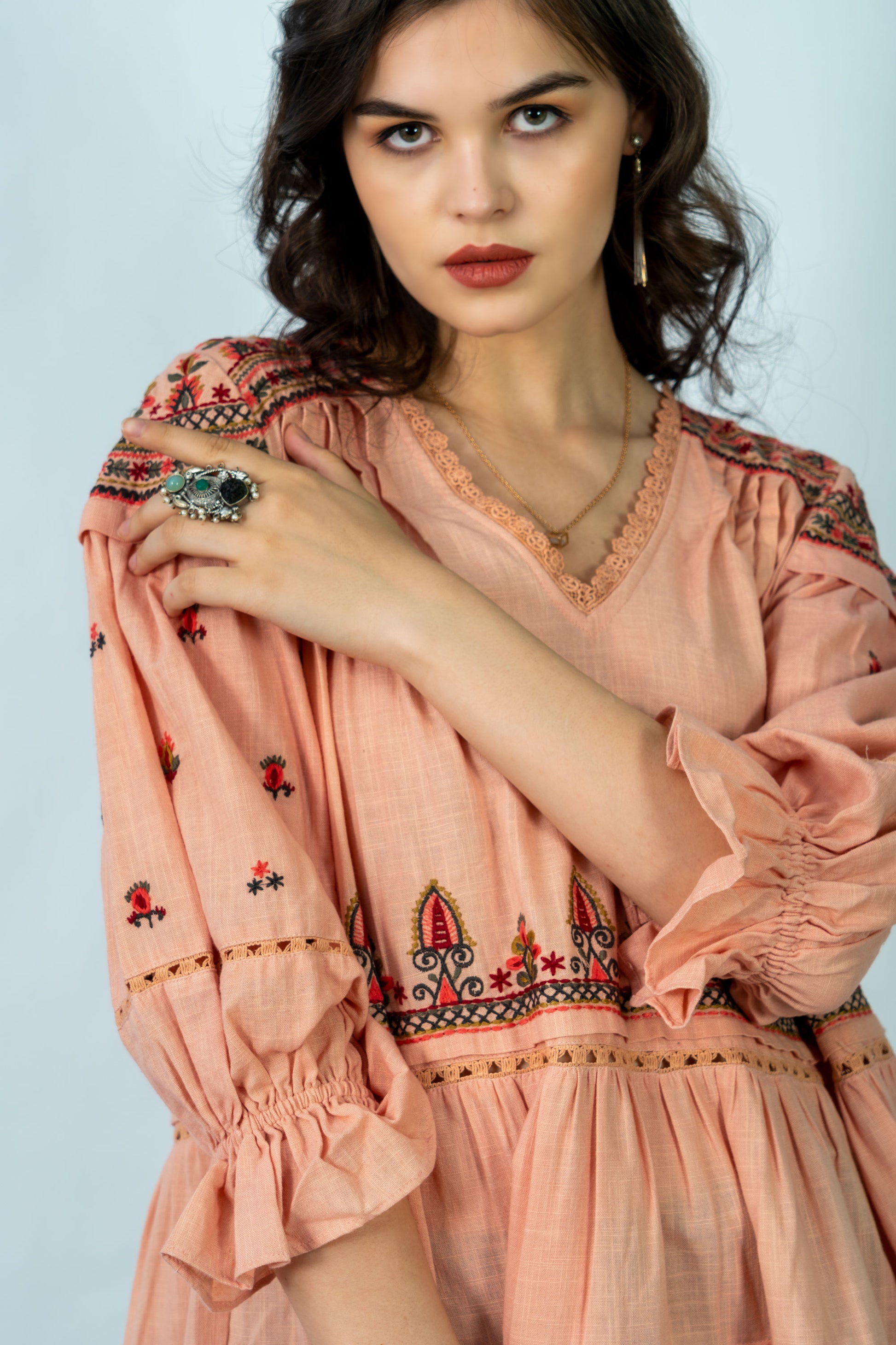Woman wearing a peach-colored dress with intricate patterns on a light blue background