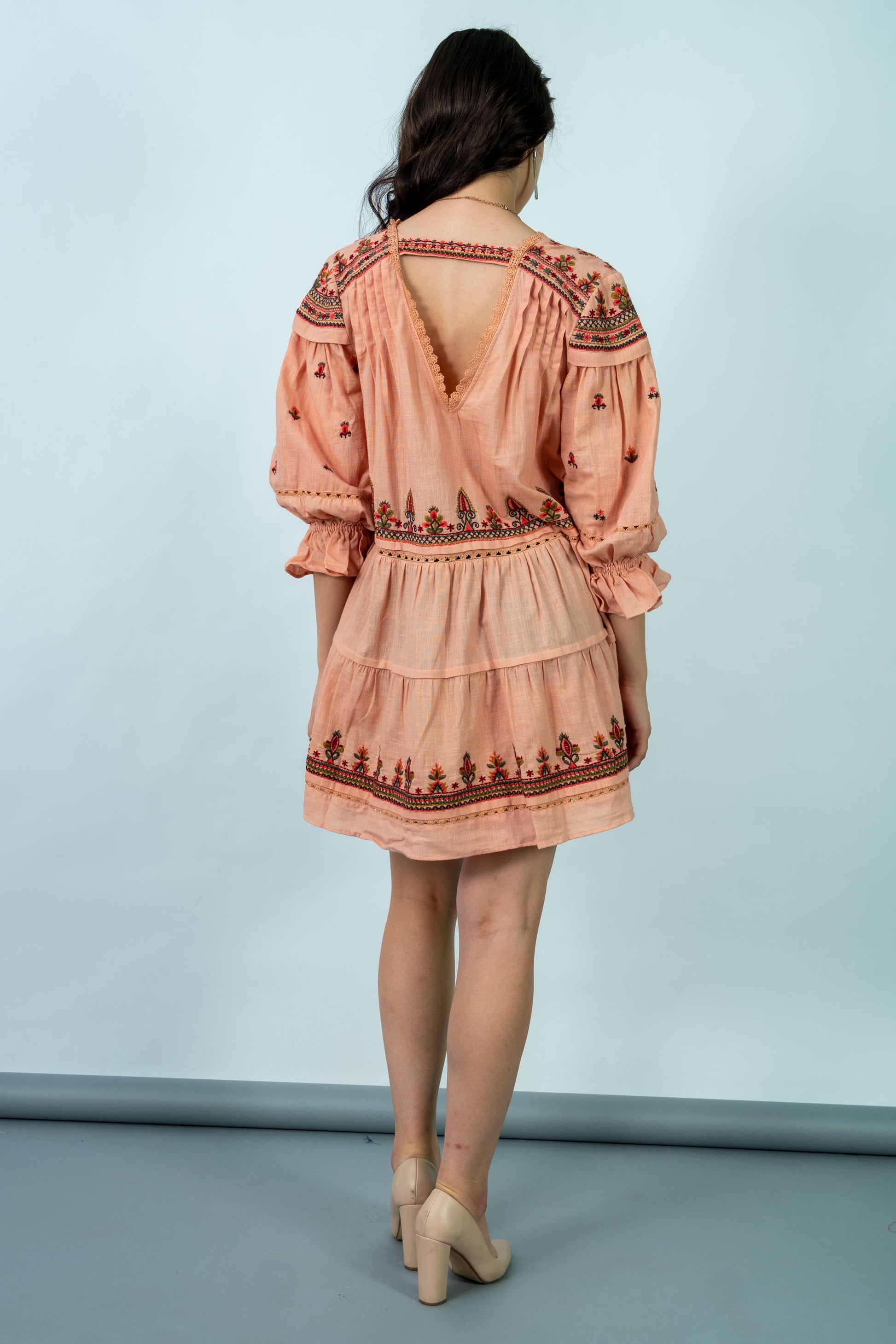 Woman wearing a peach-colored dress with intricate patterns on a light blue background