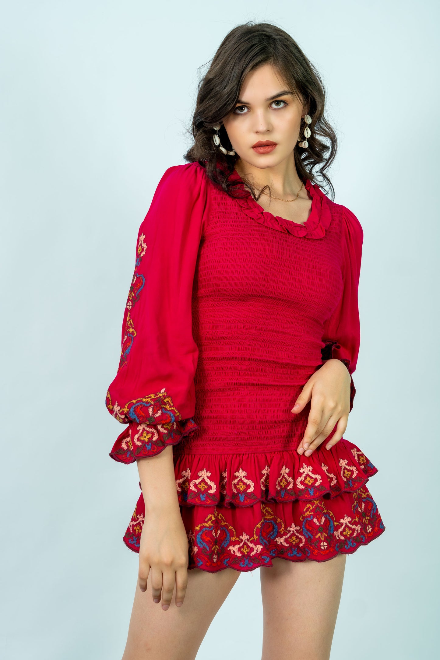 Woman wearing a red dress with floral embroidery on a light gray background