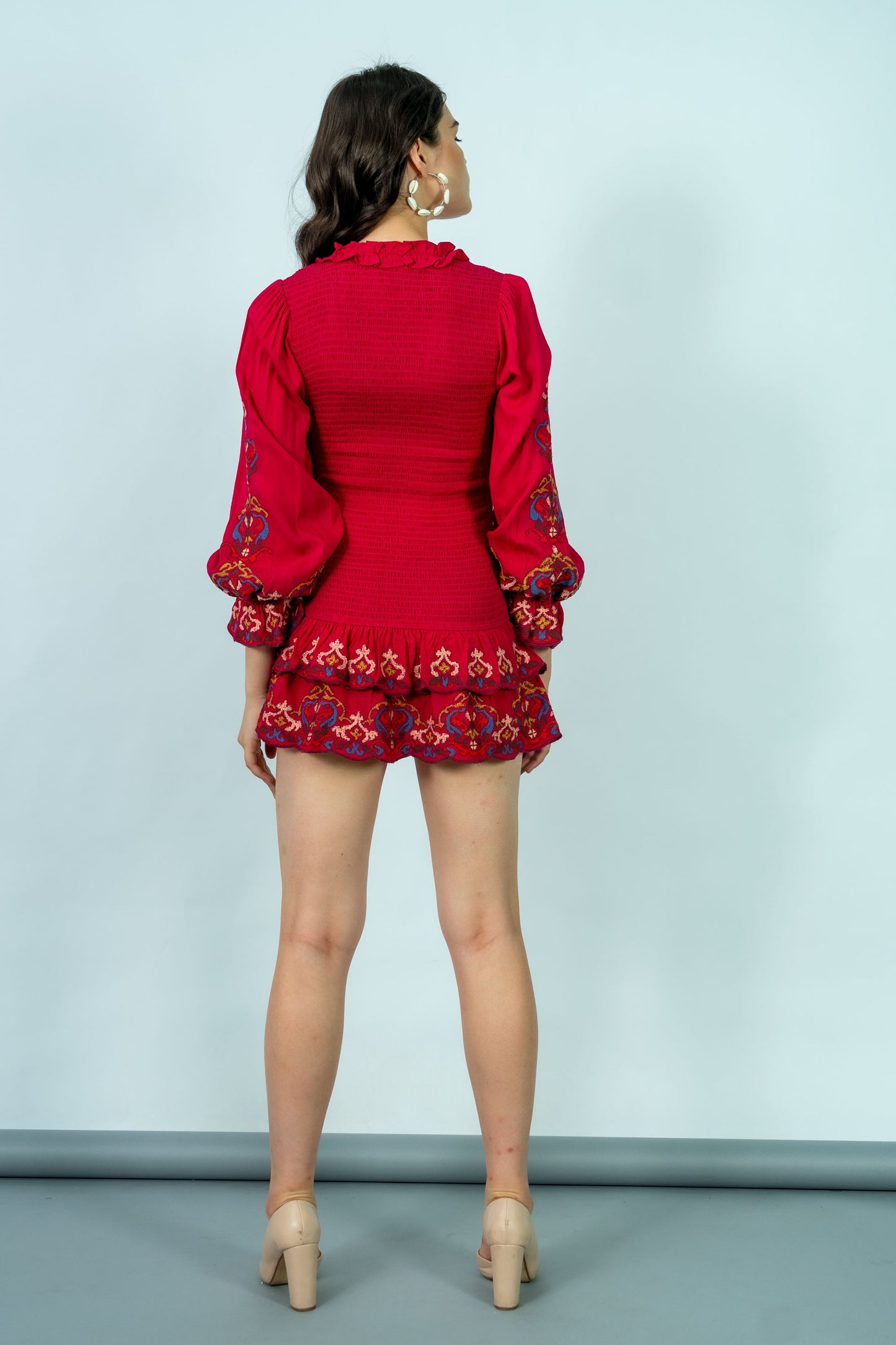 Woman wearing a red outfit with floral embroidery on a light blue background