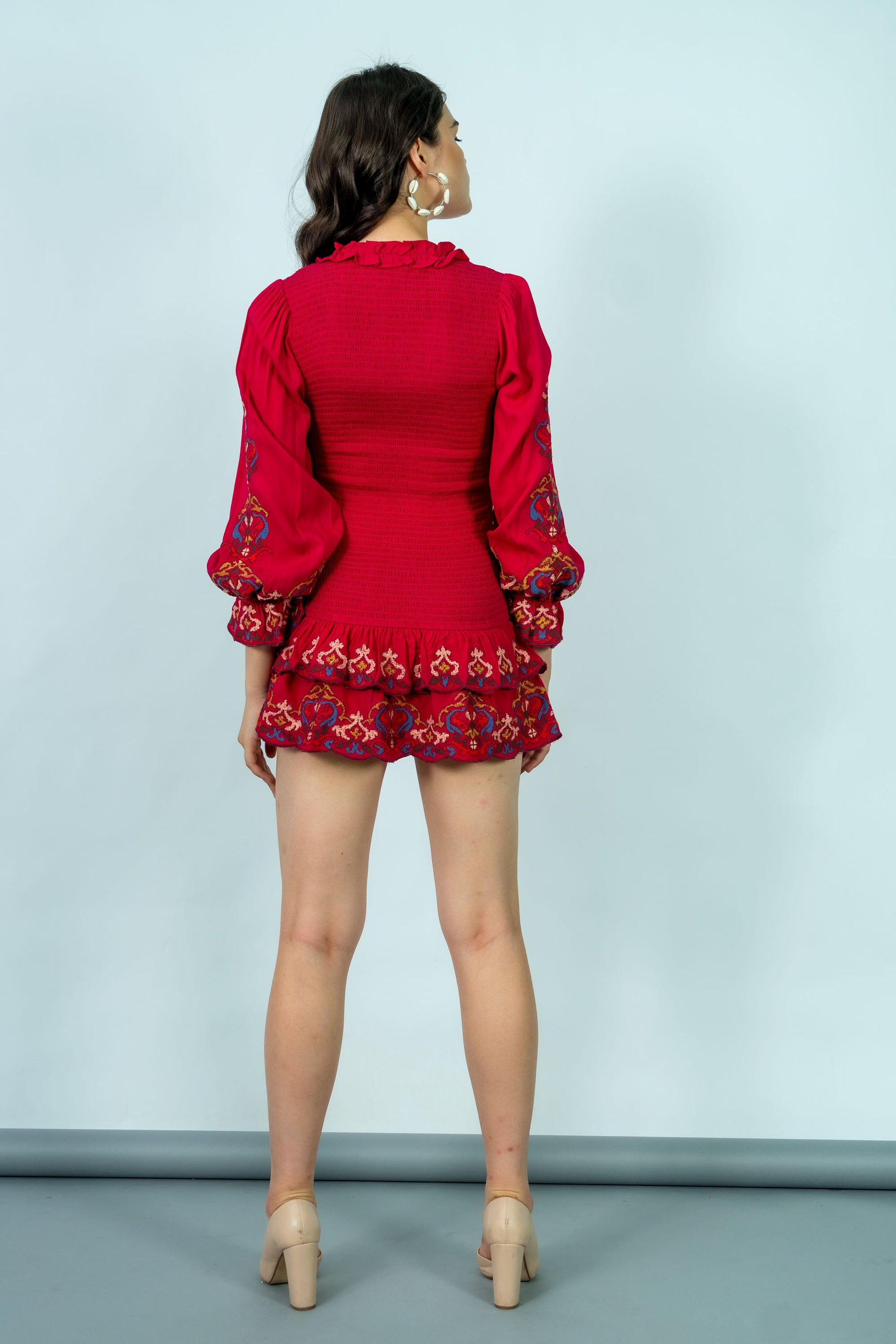 Woman wearing a red outfit with floral embroidery on a light blue background