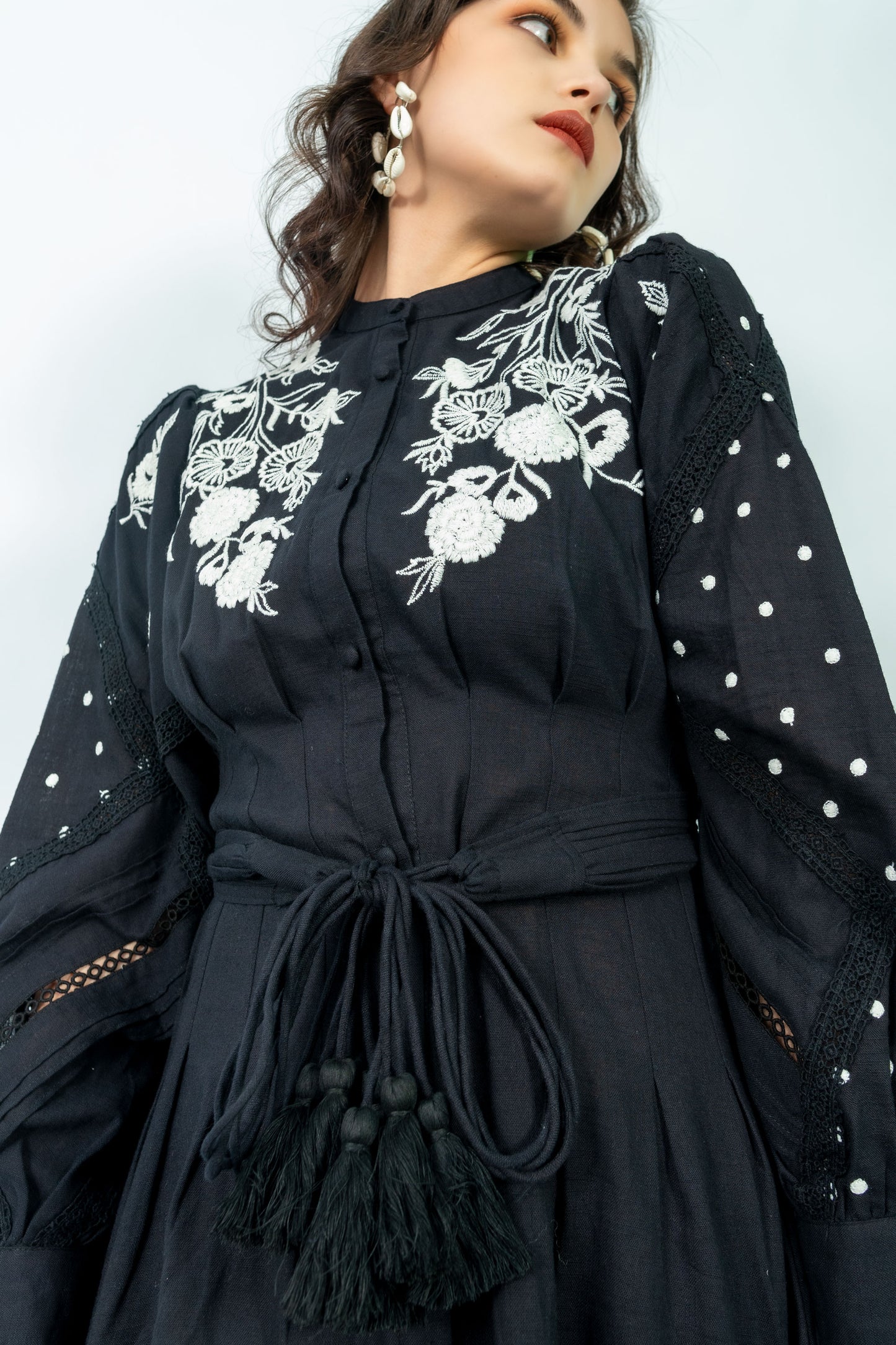 Woman wearing a black dress with white floral embroidery against a light blue background