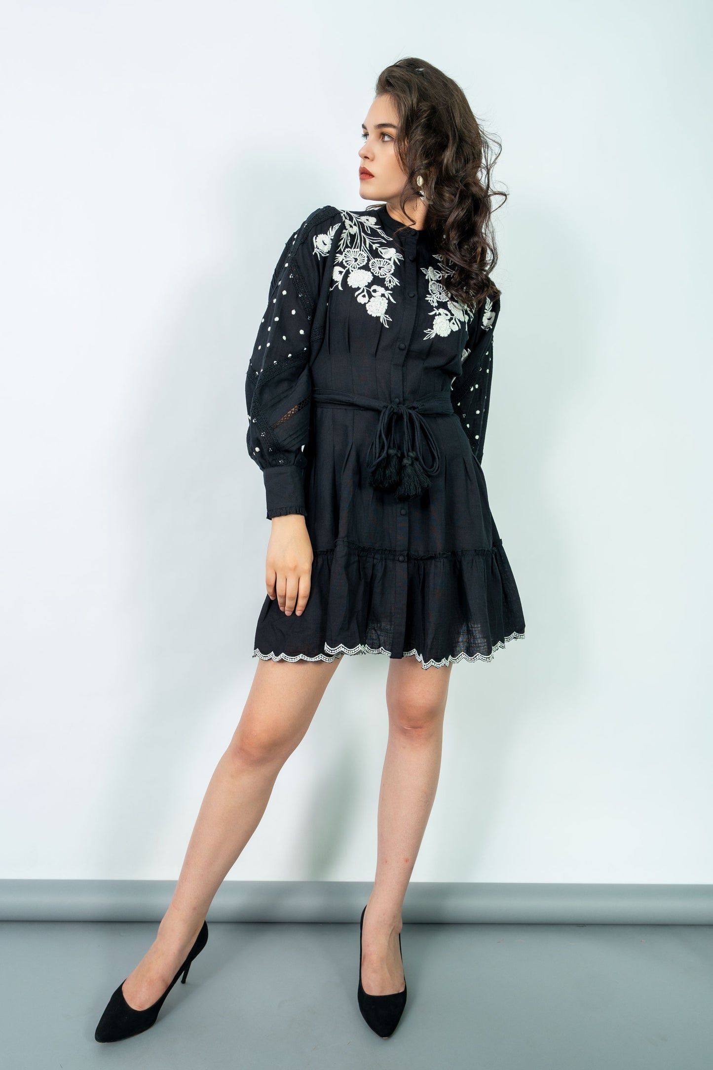 Woman wearing a black dress with white floral embroidery against a light gray background