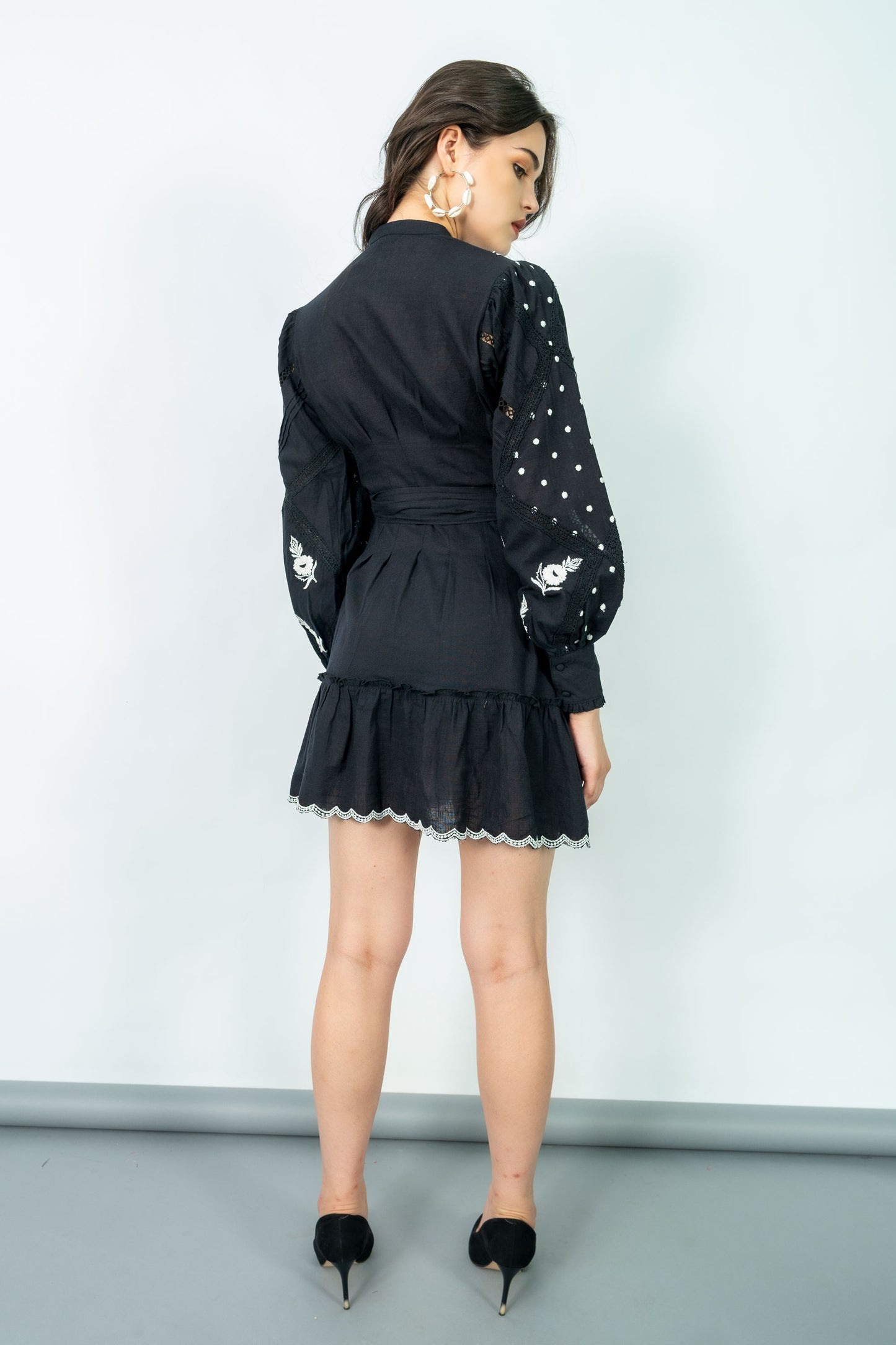 Woman wearing a black dress with white lace details against a plain background