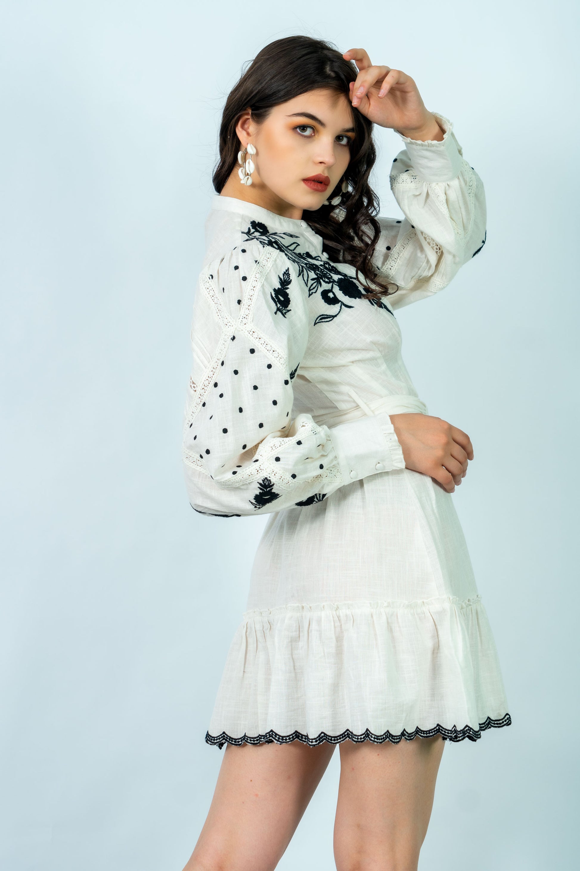 Woman wearing a white dress with black embroidery on a light blue background