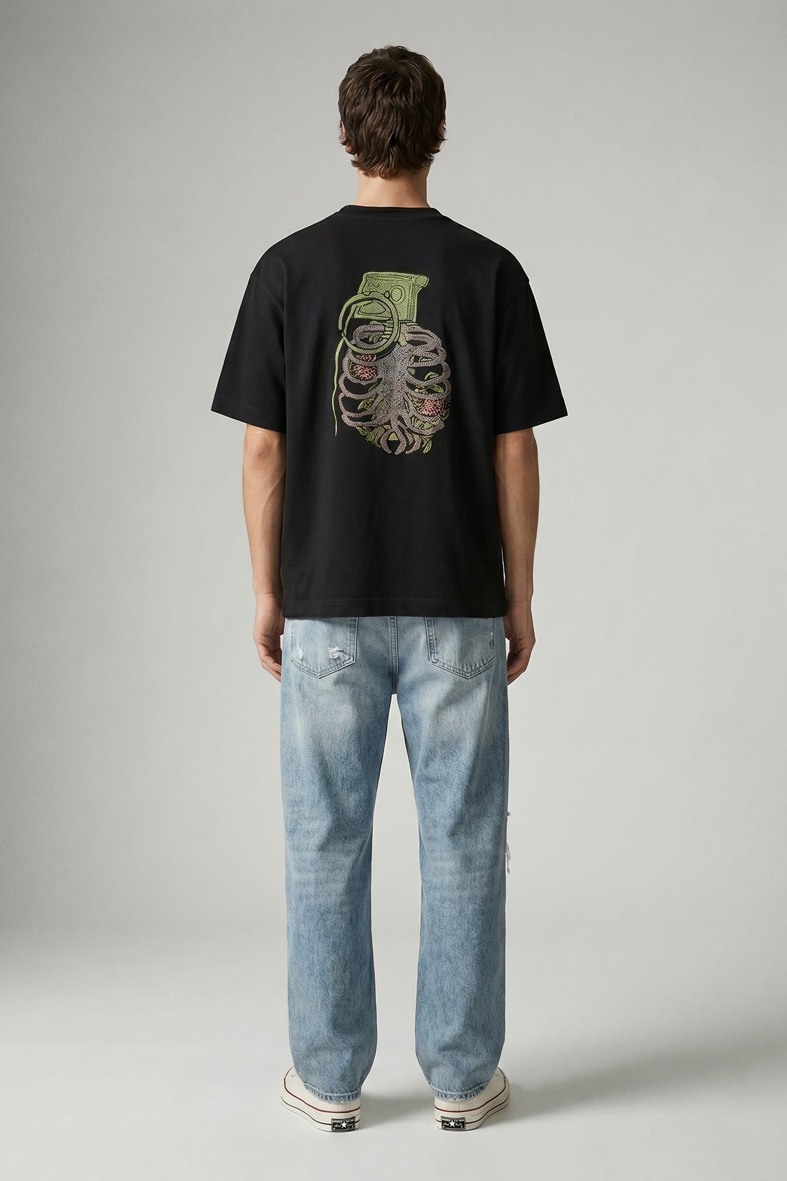 Person wearing a black t-shirt with a graphic design on the back and light blue jeans, standing against a plain background.