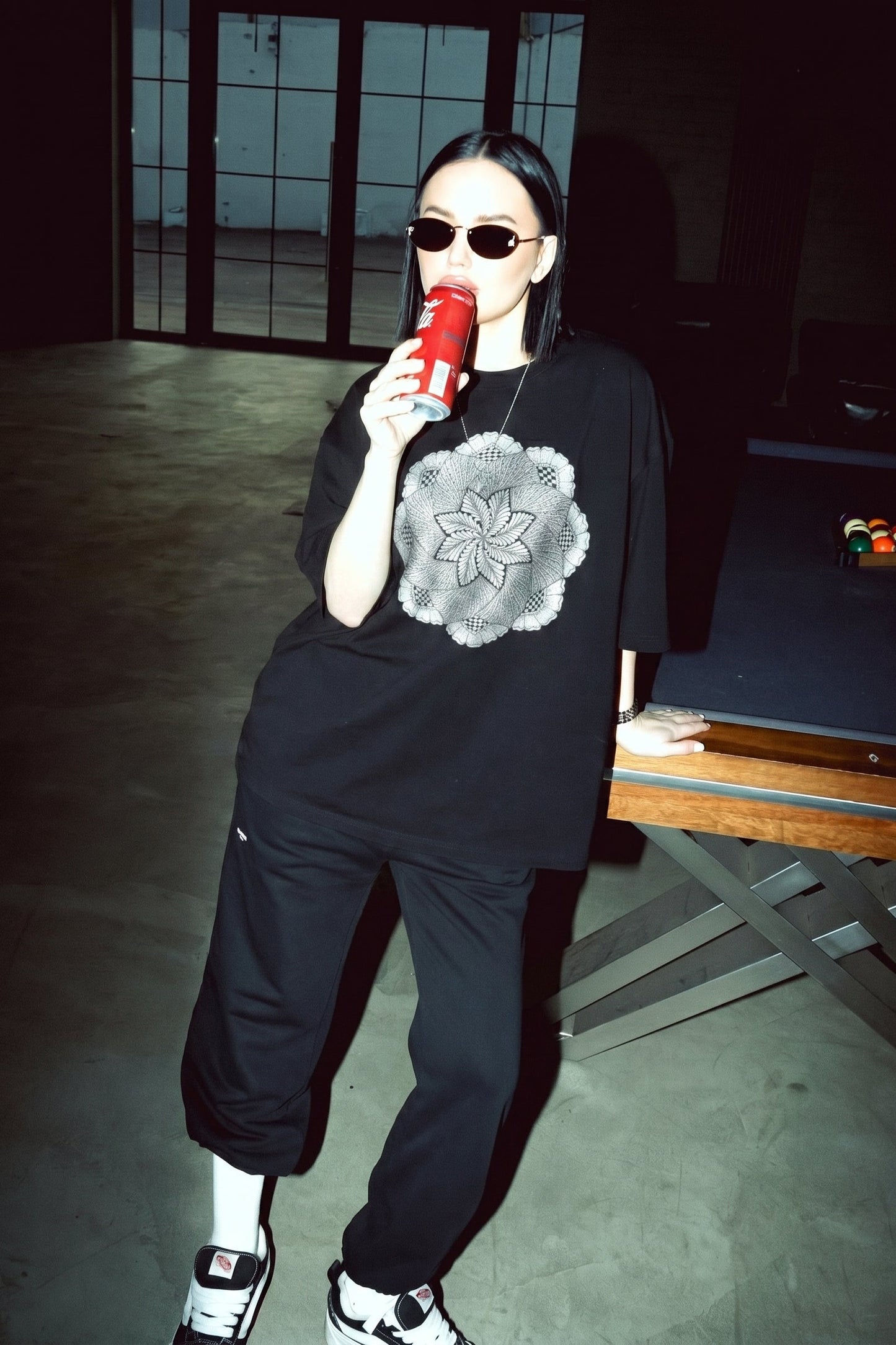 Person wearing a black outfit with a graphic design, holding a red cup in a dimly lit room.