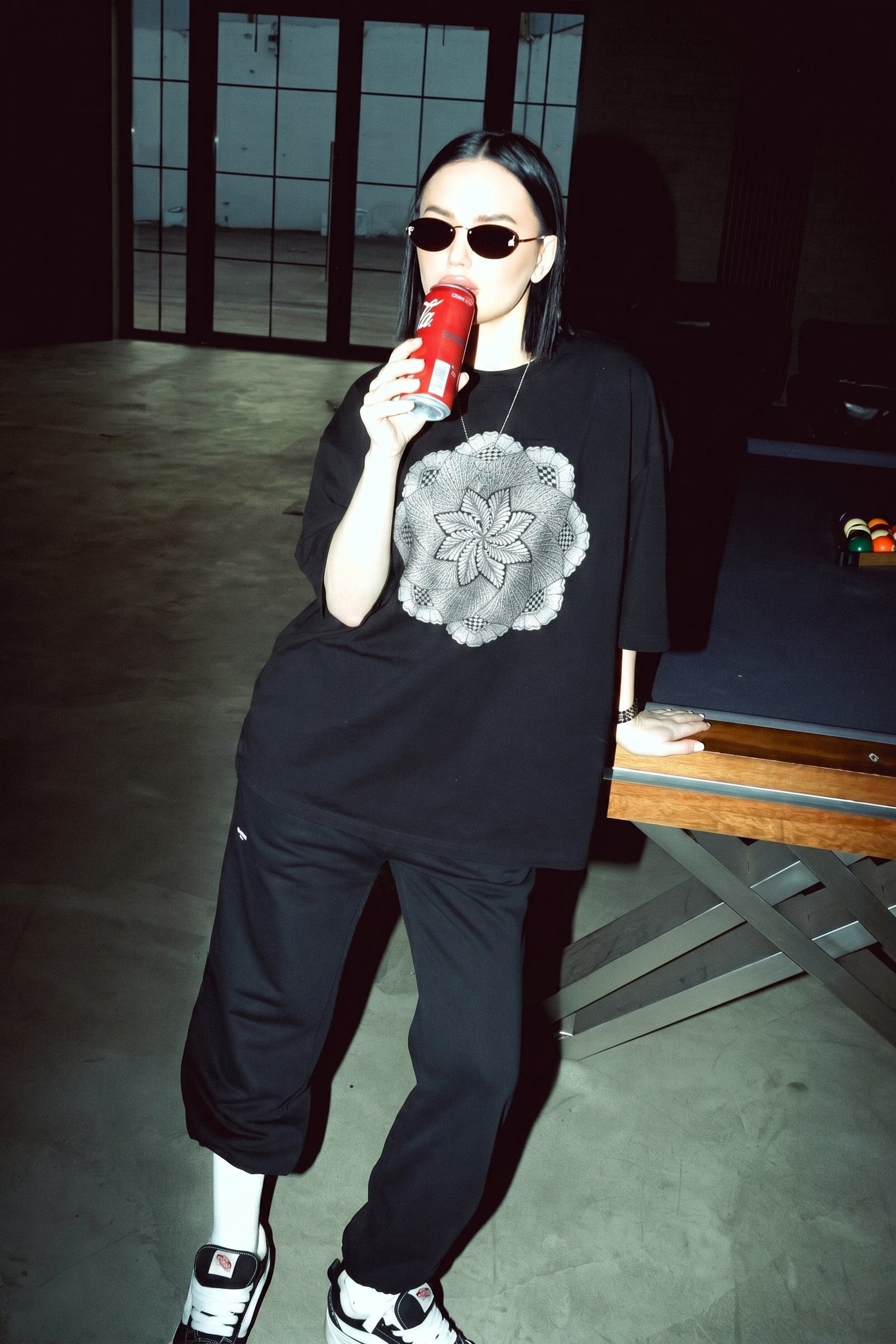 Person wearing a black outfit with a graphic design, holding a red cup in a dimly lit room.