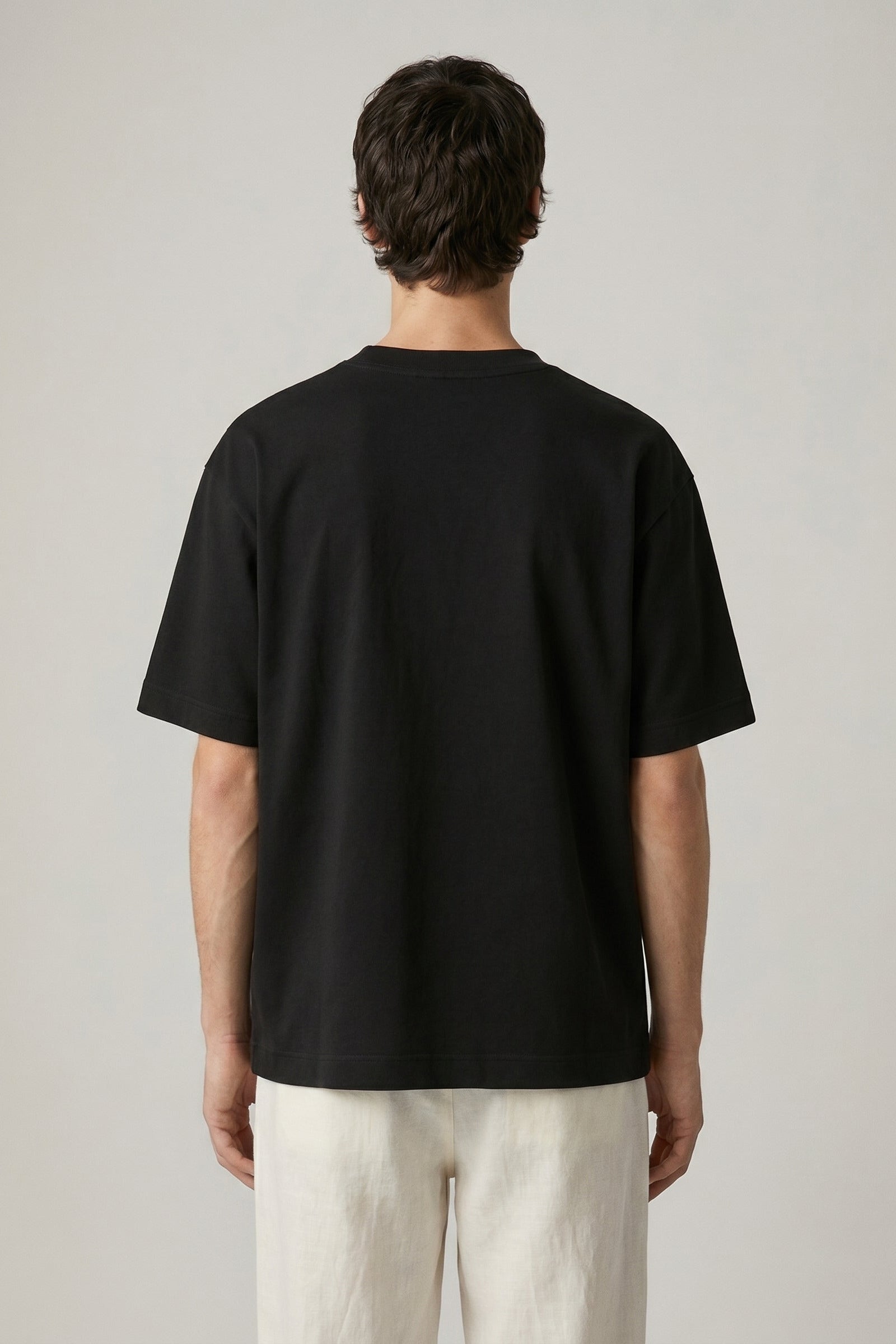 Person wearing a black t-shirt and light-colored pants on a plain background