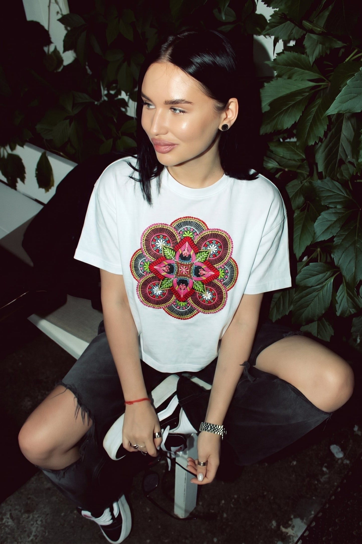 Woman wearing a white t-shirt with a colorful floral design, sitting outdoors.
