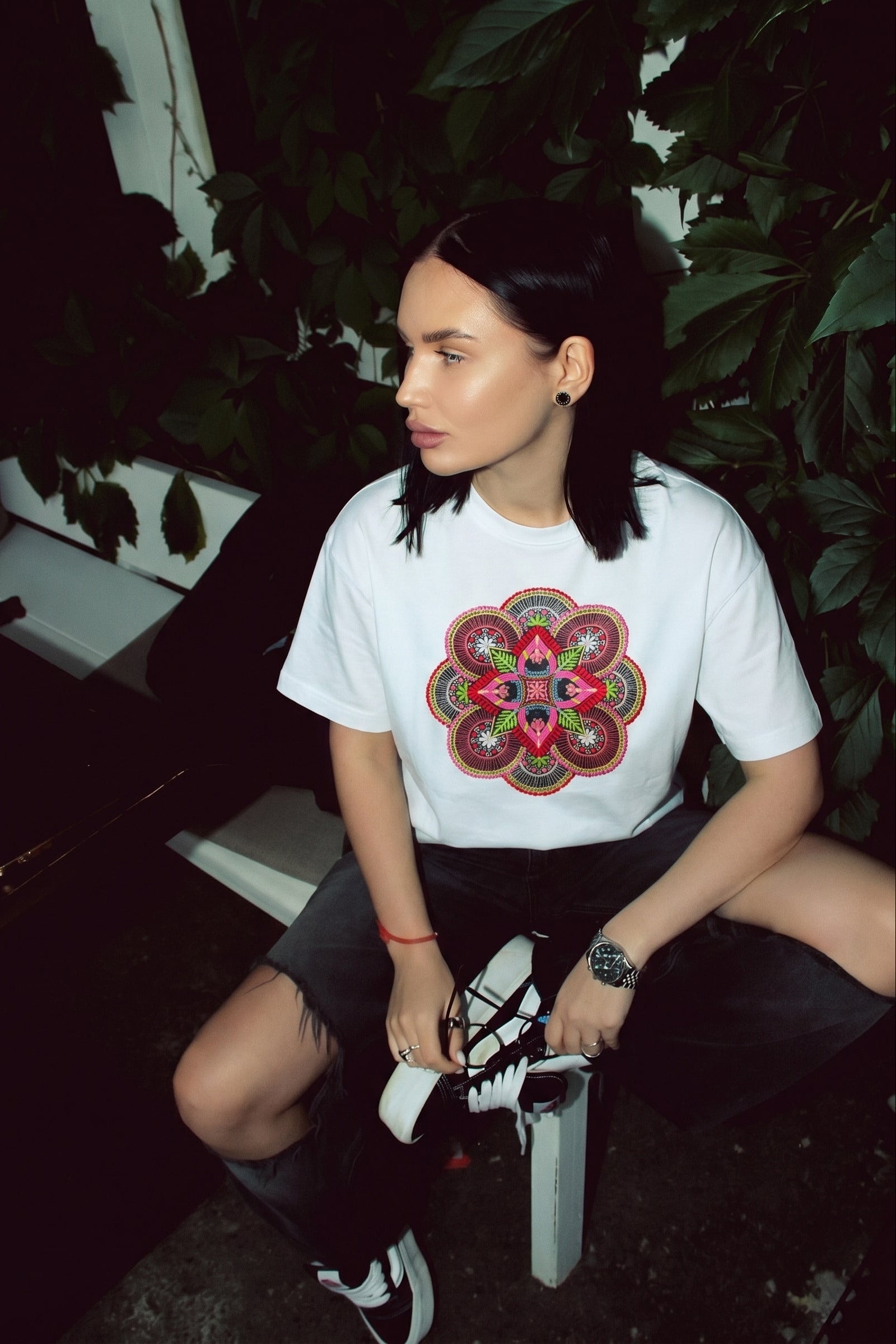 Person wearing a white t-shirt with a colorful geometric design, sitting outdoors.