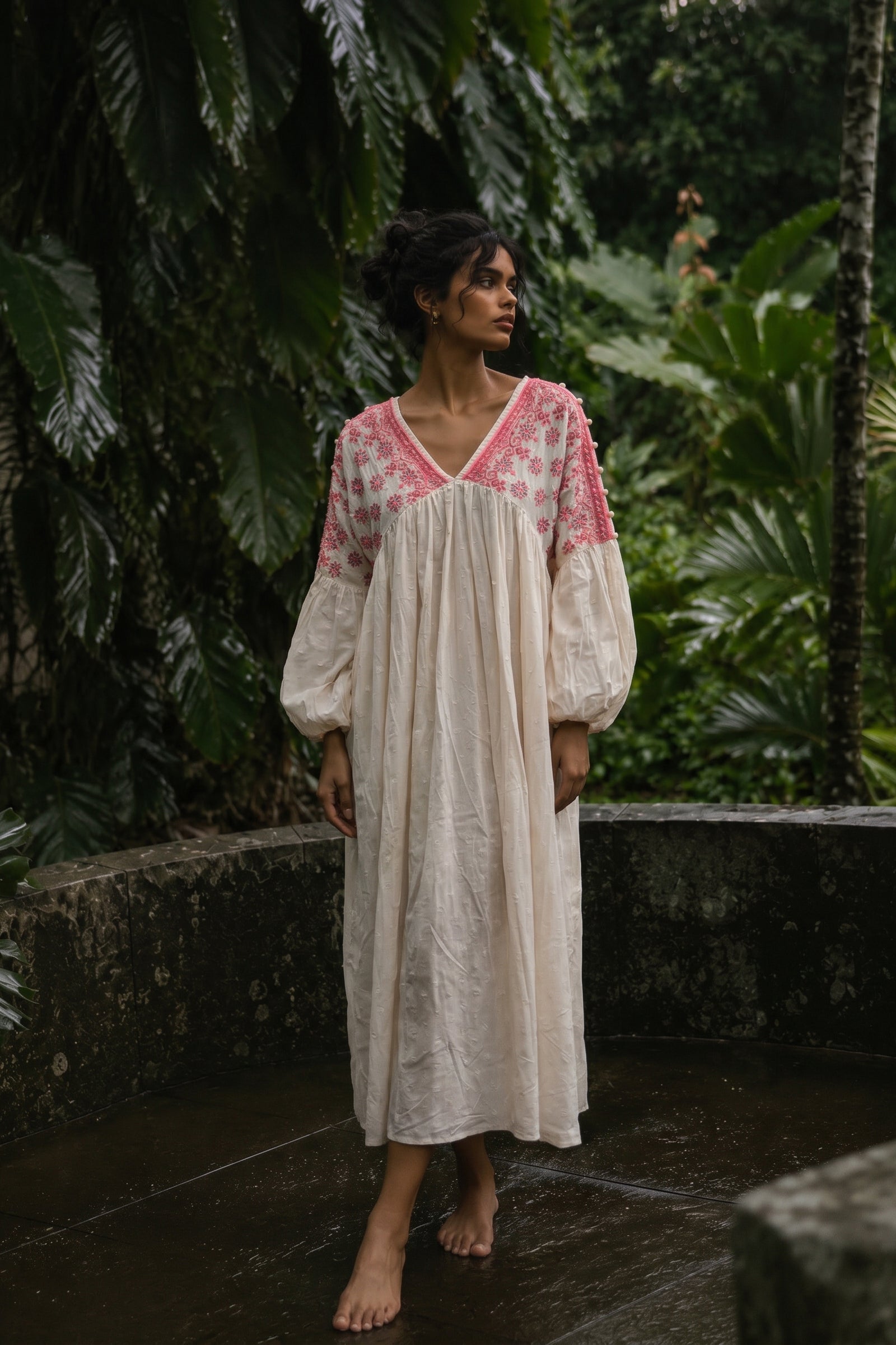 Woman wearing a long, light-colored dress with pink floral patterns in a tropical setting.