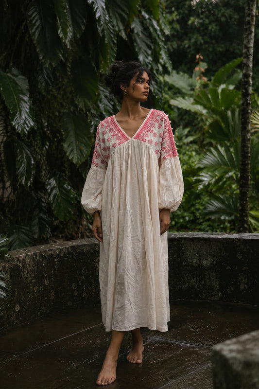Woman wearing a long, light-colored dress with pink floral patterns in a tropical setting.