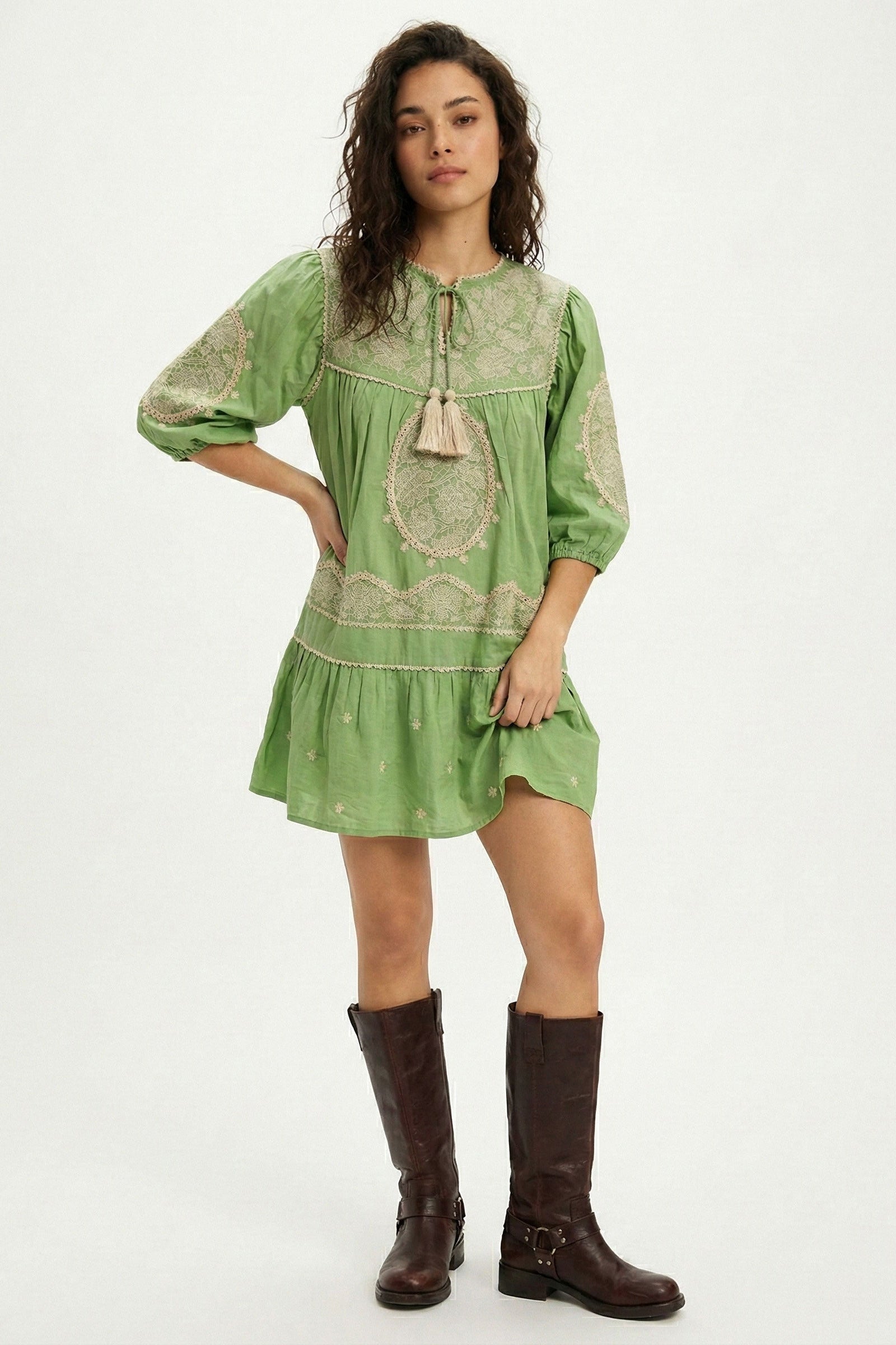 Woman wearing a green dress with lace details and brown boots on a white background
