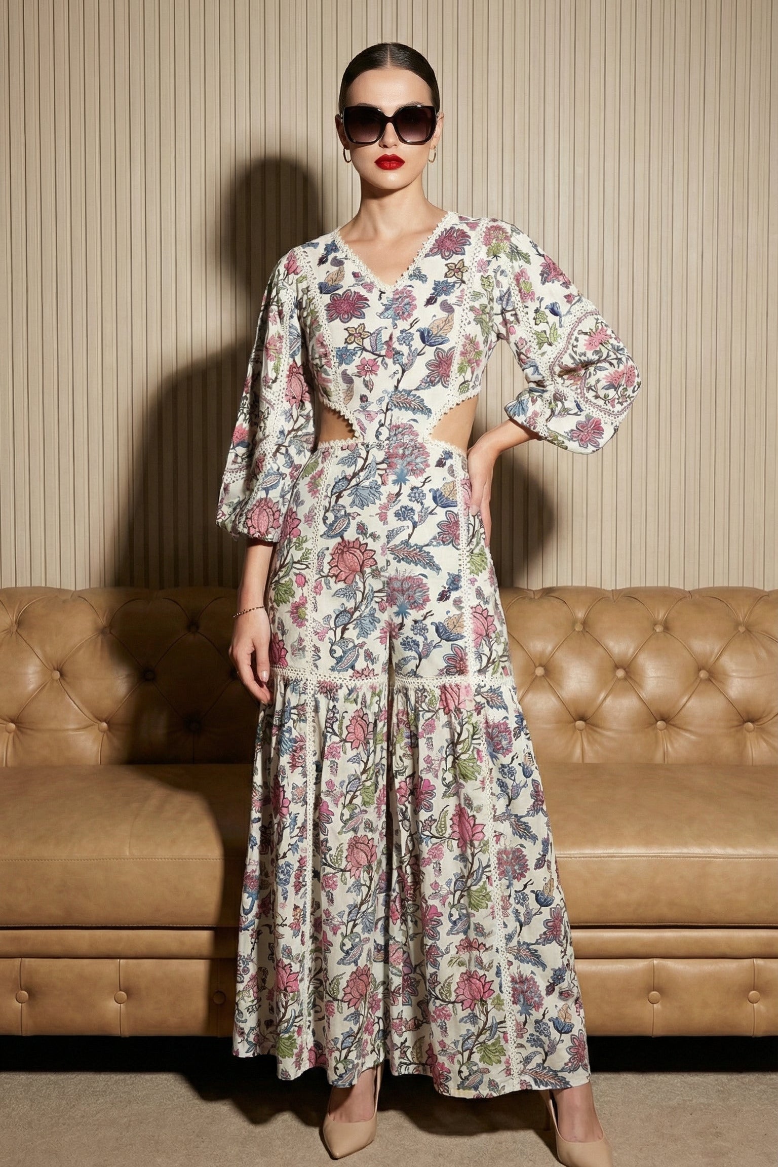 Woman wearing a floral dress standing in front of a brown sofa with a striped wall background.