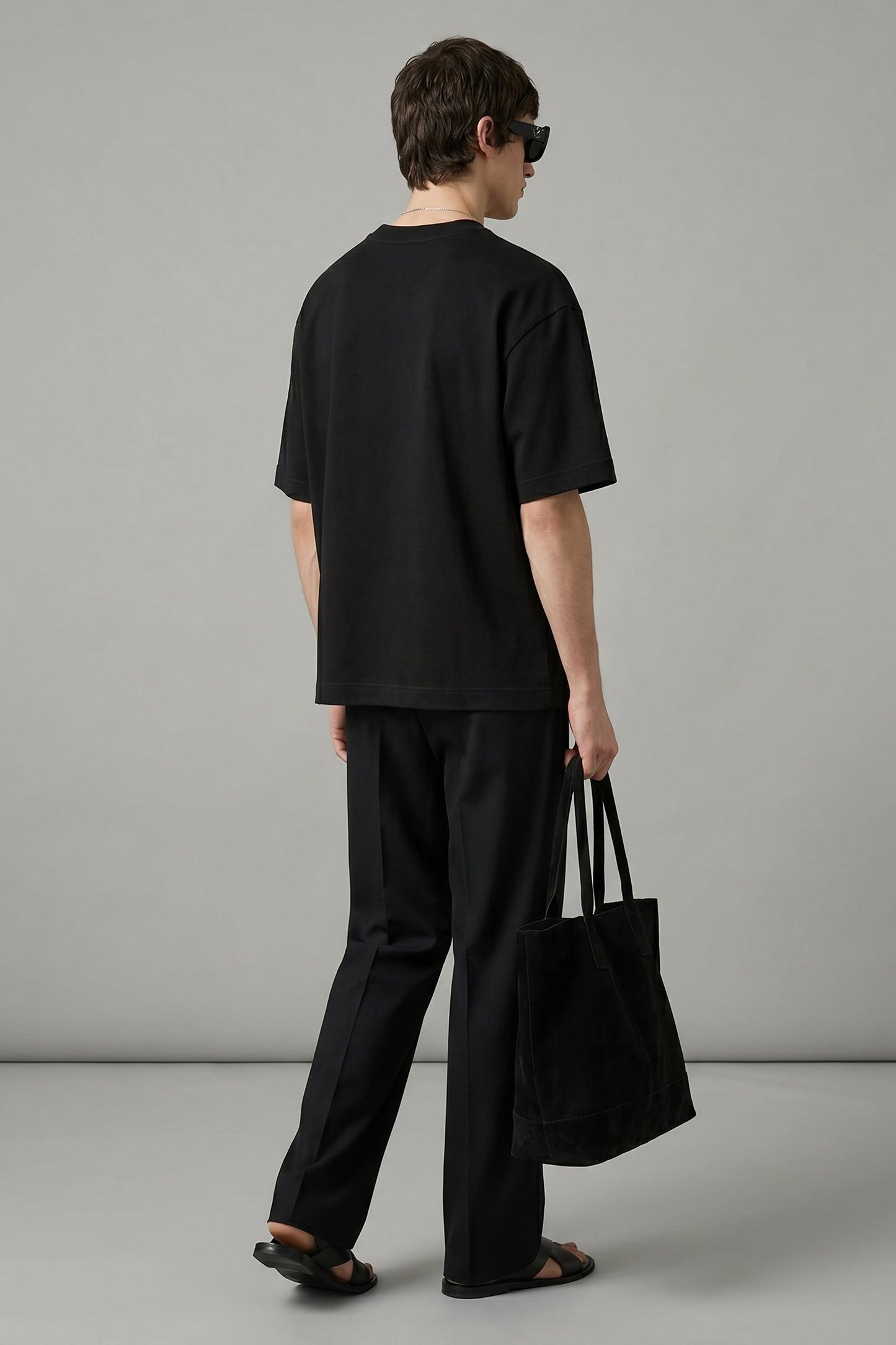 Person wearing a black outfit holding a black bag against a gray background