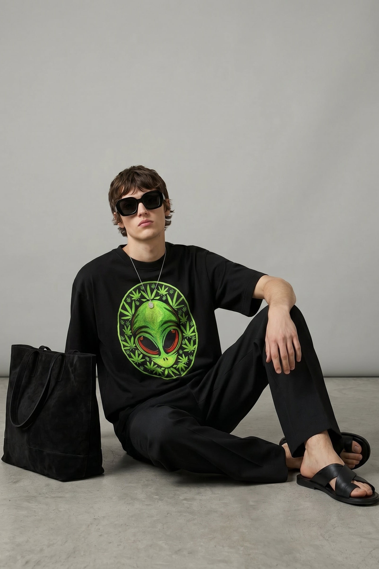 Person wearing a black t-shirt with an alien design, sitting on the floor against a gray background.