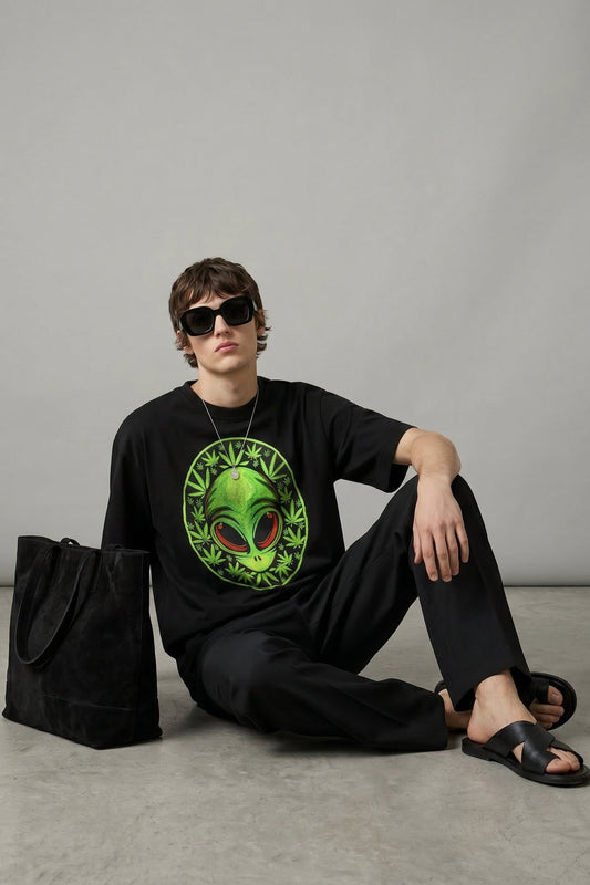 Person wearing a black t-shirt with an alien design, sitting on the floor against a gray background.