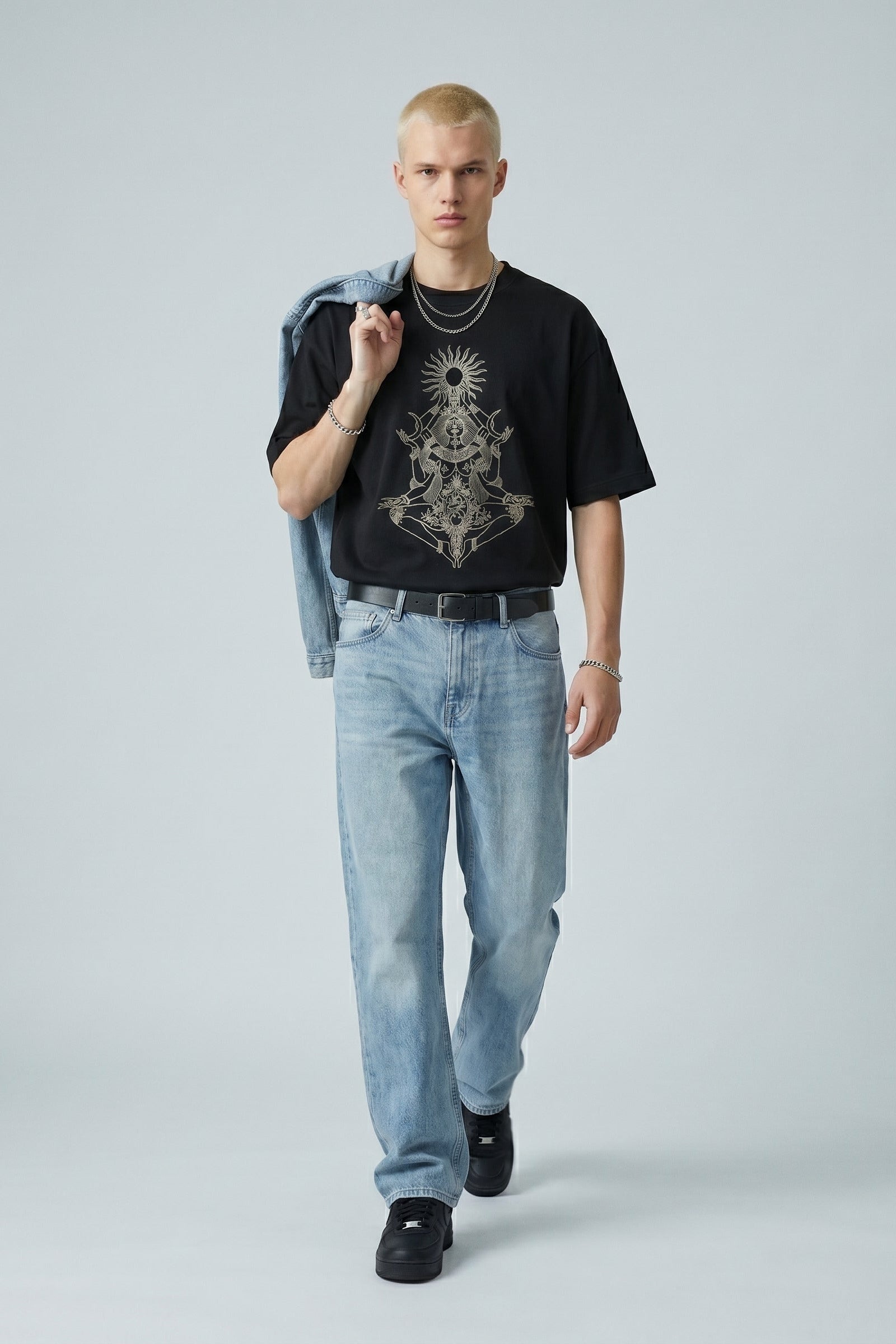 Man wearing a black t-shirt with graphic design, light blue jeans, and black shoes on a gray background