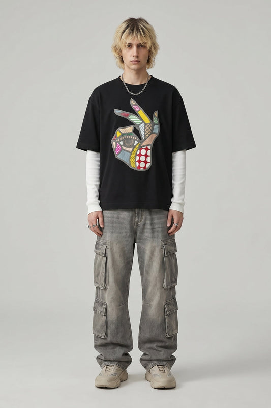 Person wearing a black t-shirt with a colorful graphic design and gray cargo pants on a plain background