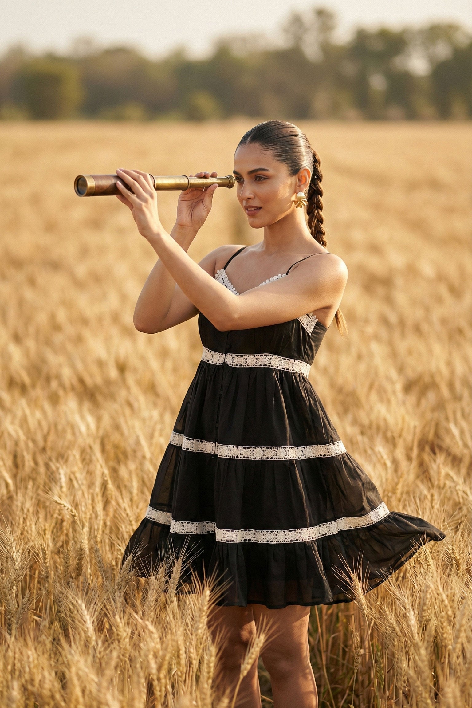 Woman in a black dress holding a vintage telescope in a golden field