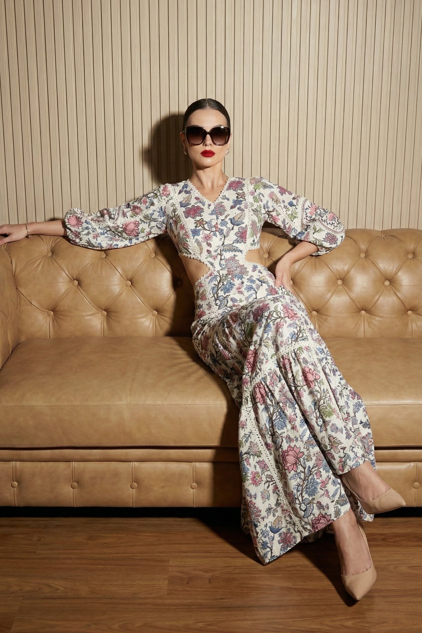 Woman in a floral dress sitting on a brown leather couch against a striped wall.