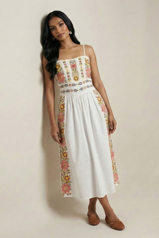 Woman wearing a white dress with floral embroidery on a plain background
