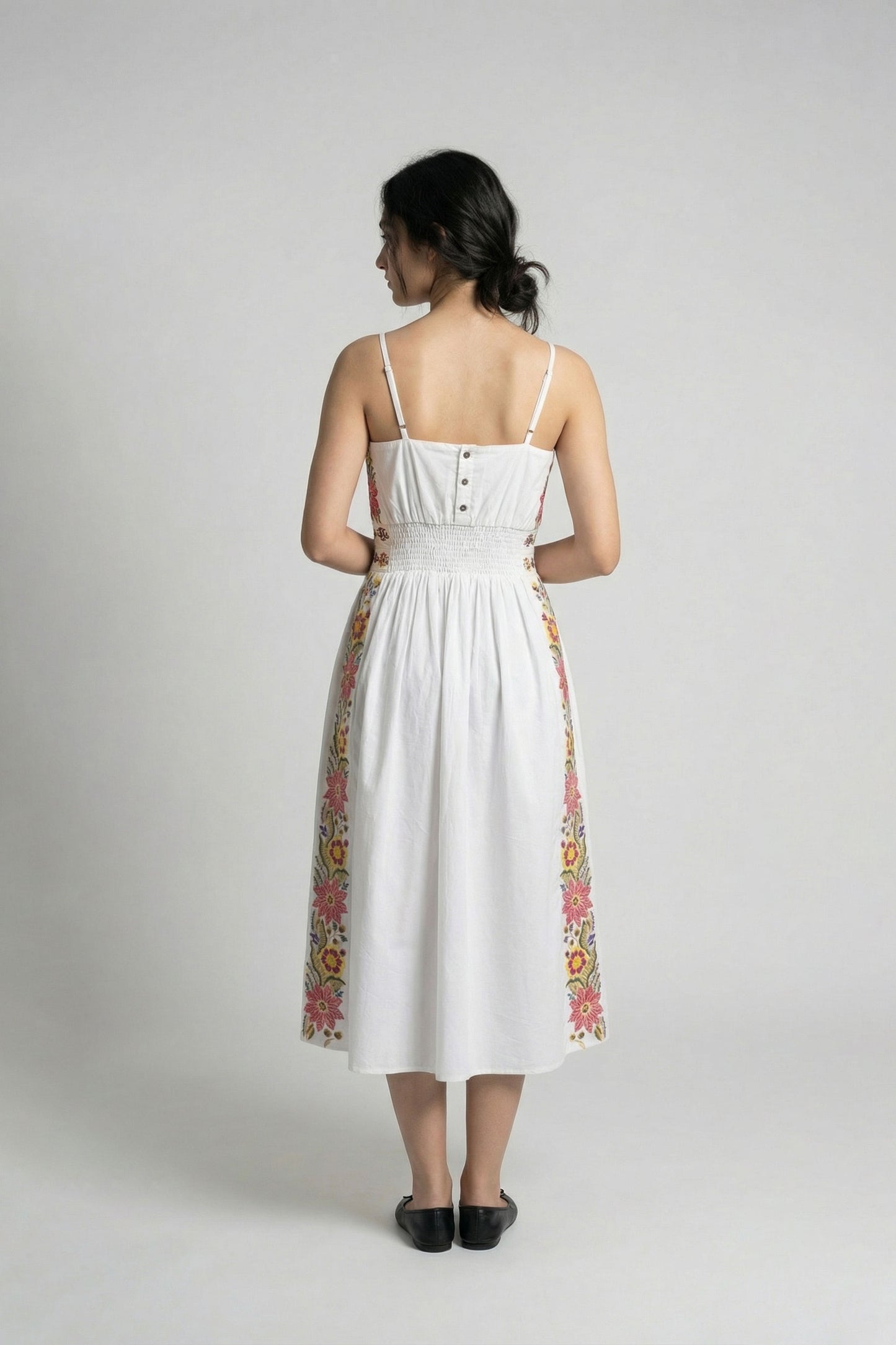 Woman wearing a white dress with colorful embroidery on a plain background