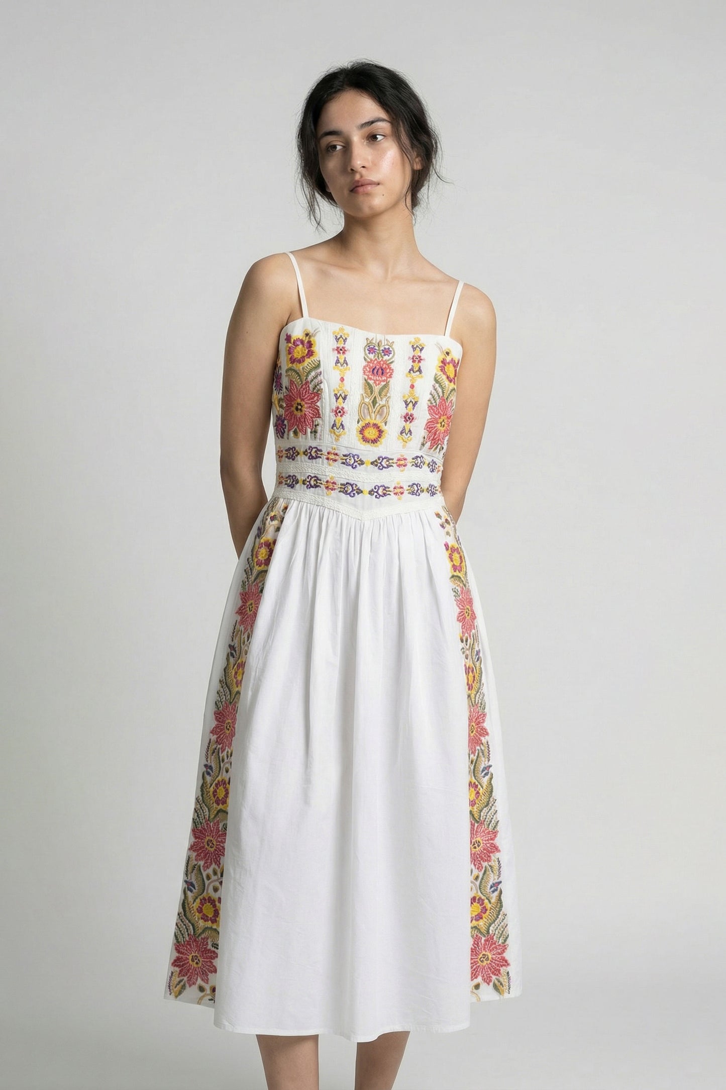 Woman wearing a white dress with colorful floral patterns on a plain background