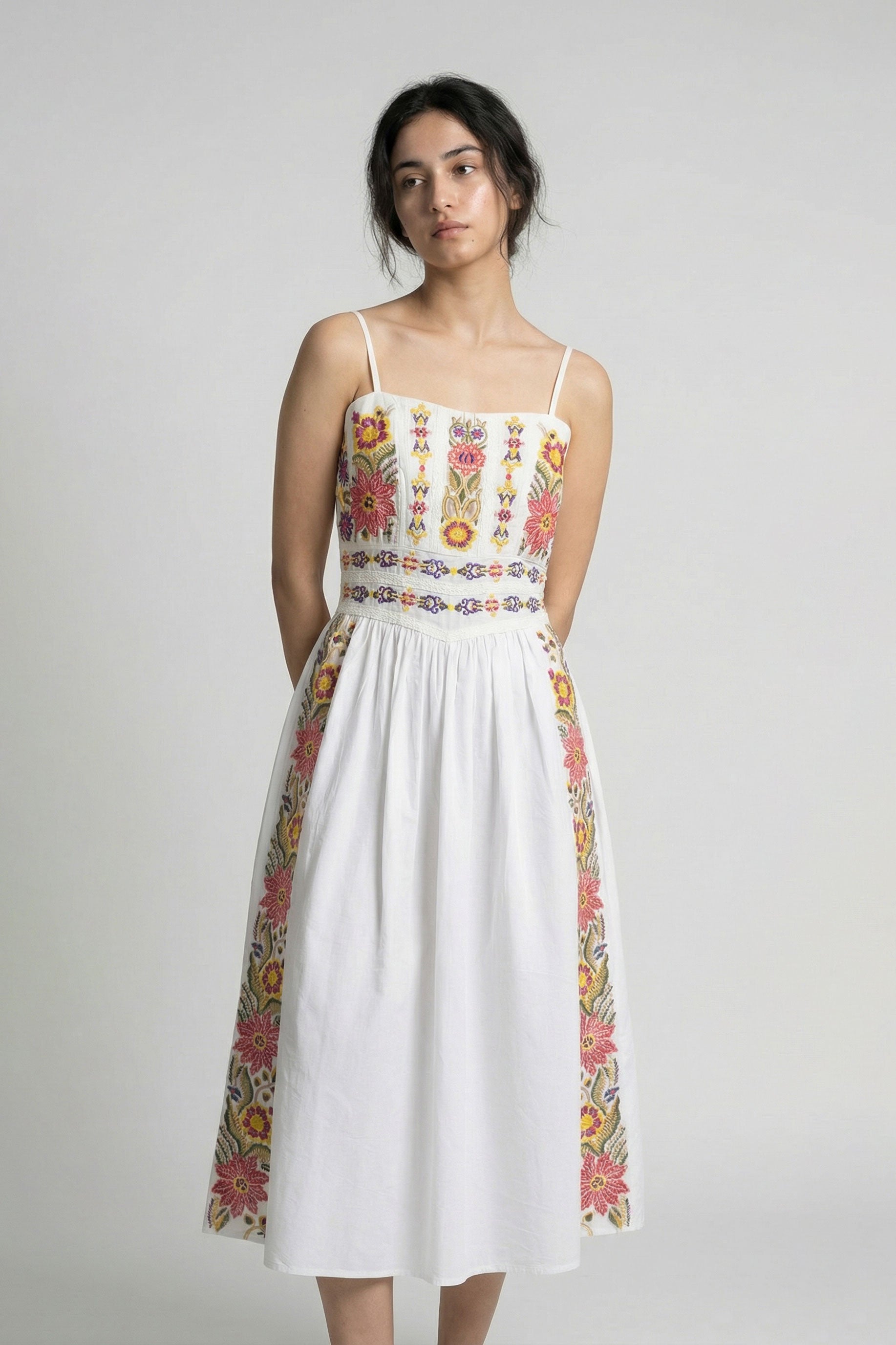 Woman wearing a white dress with colorful floral patterns on a plain background