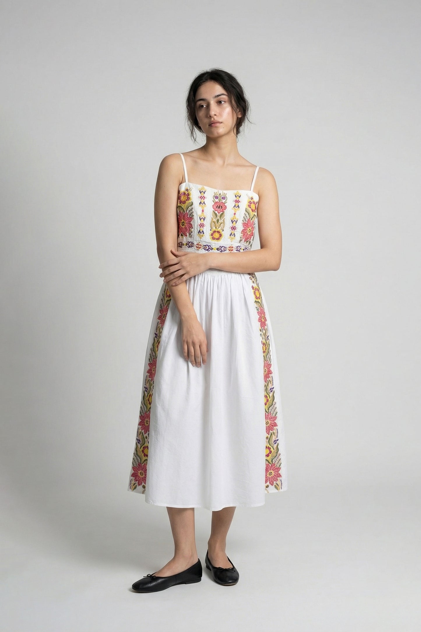 Woman wearing a white dress with colorful floral patterns on a plain background
