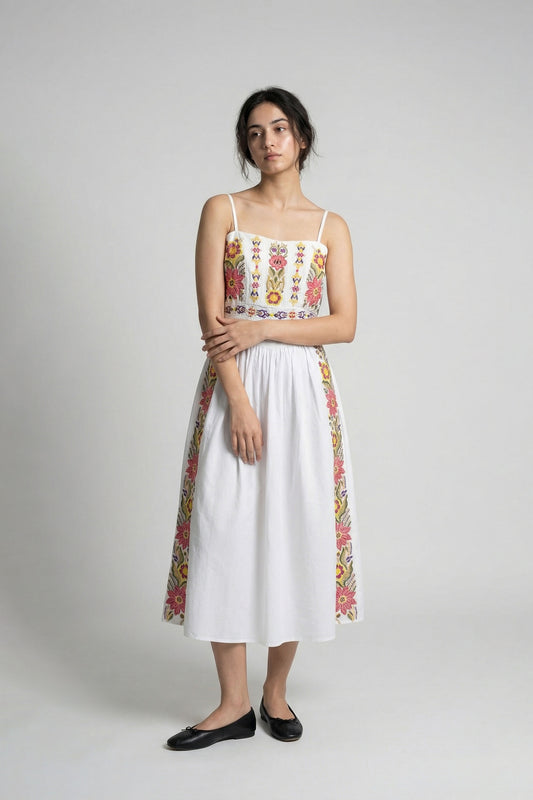Woman wearing a white dress with colorful floral patterns on a plain background