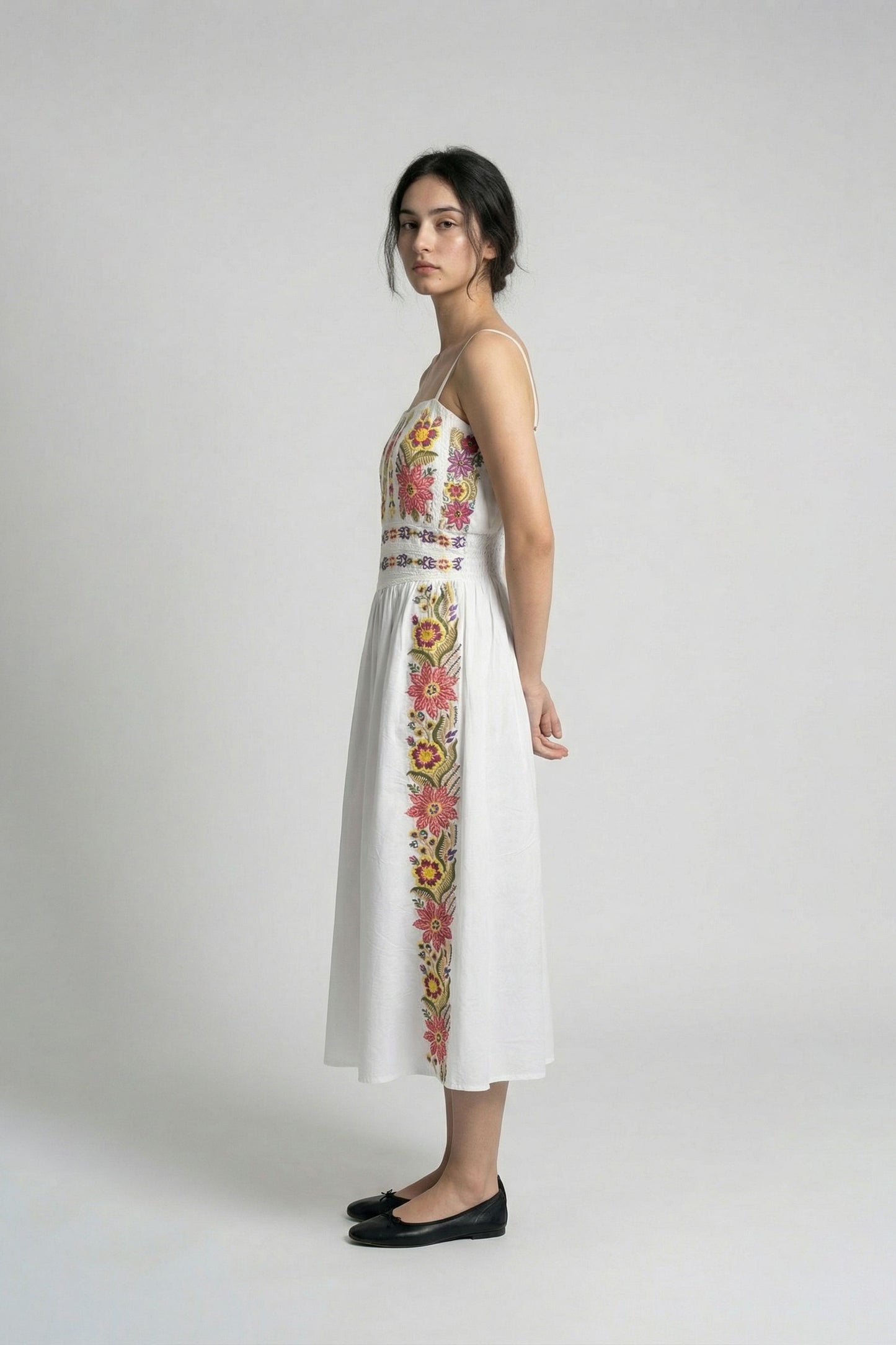 Woman wearing a white dress with floral embroidery on a plain background