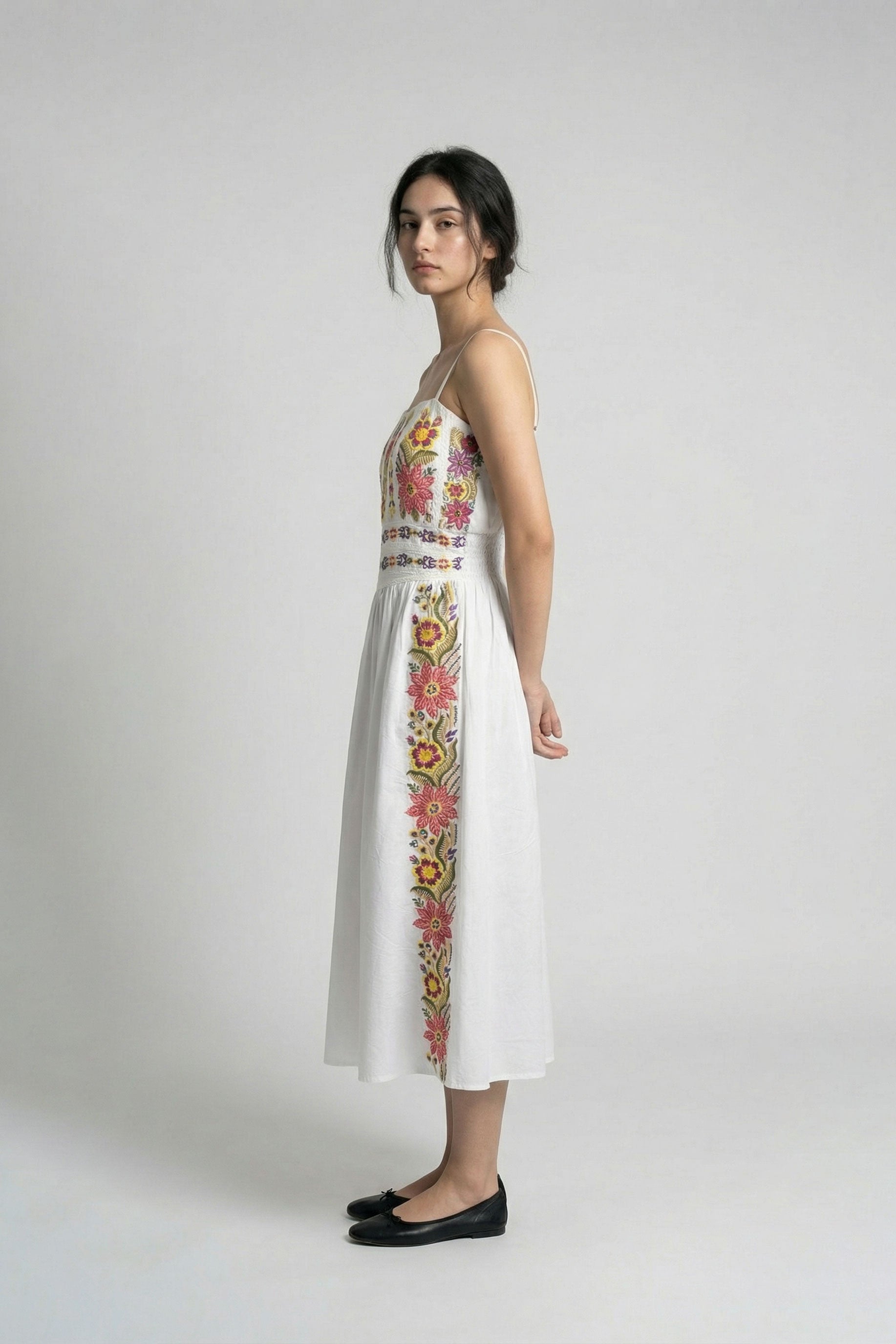 Woman wearing a white dress with floral embroidery on a plain background